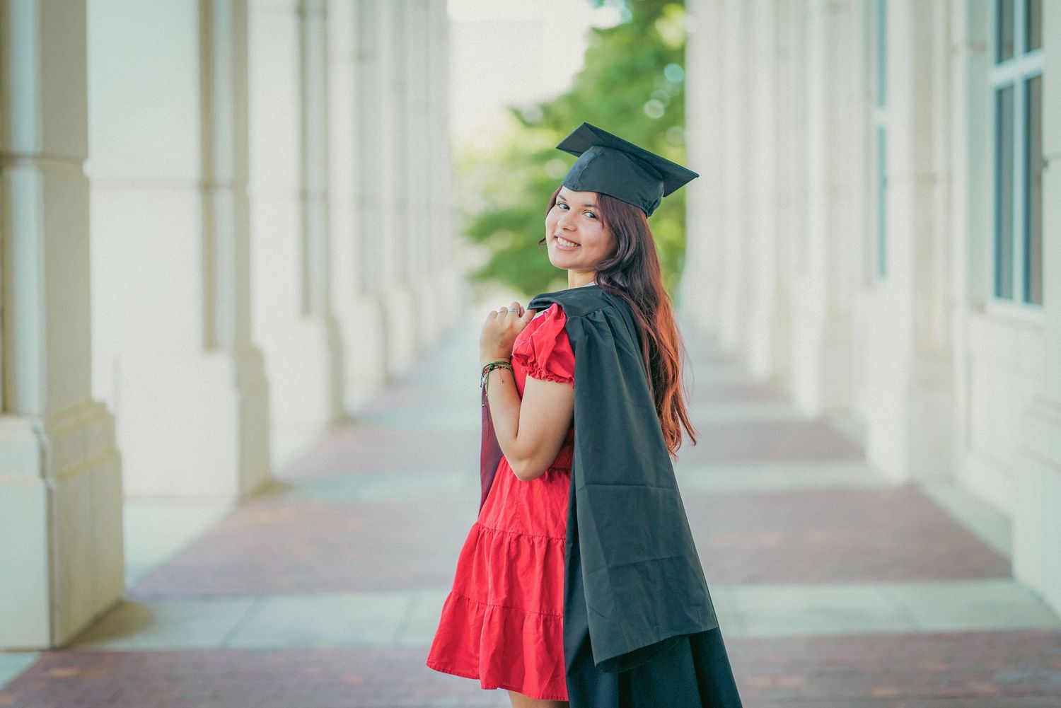 Graduate in cap and gown posing in front of white columned building.