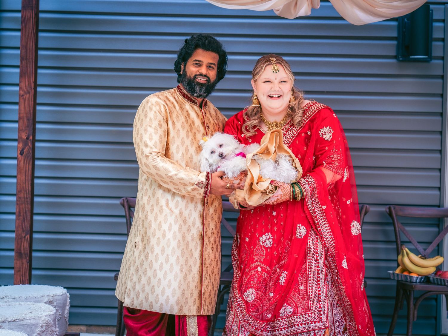 A couple in red and cream traditional attire share a moment under an outdoor wedding canopy.