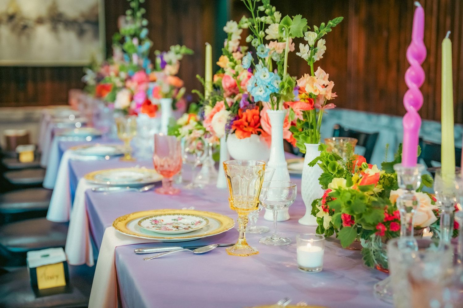 Elegant wedding reception table settings with purple linens and colorful floral centerpieces.