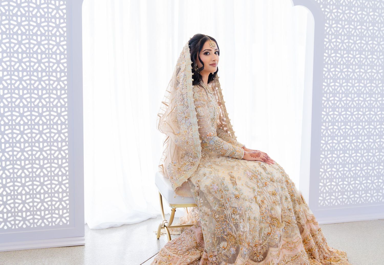 Traditional South Asian bridal attire featuring intricate gold embroidery against white lattice background.