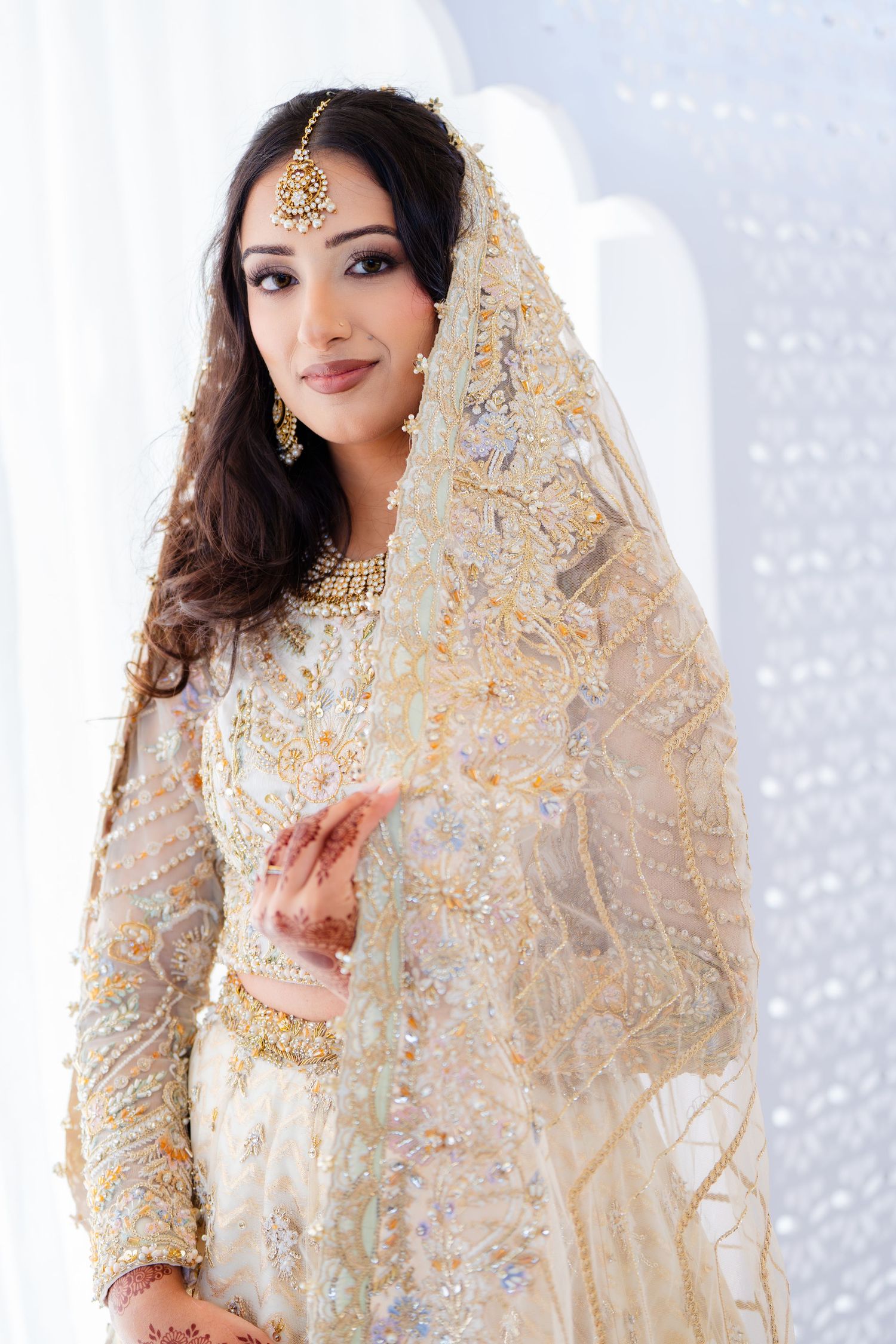 Bride in ivory and gold embroidered lehenga showing traditional mehndi designs.