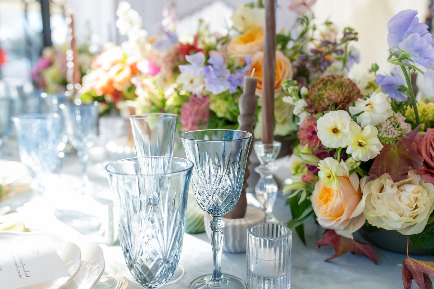 Elegant table setting with blue glassware and floral centerpieces for a wedding reception.
