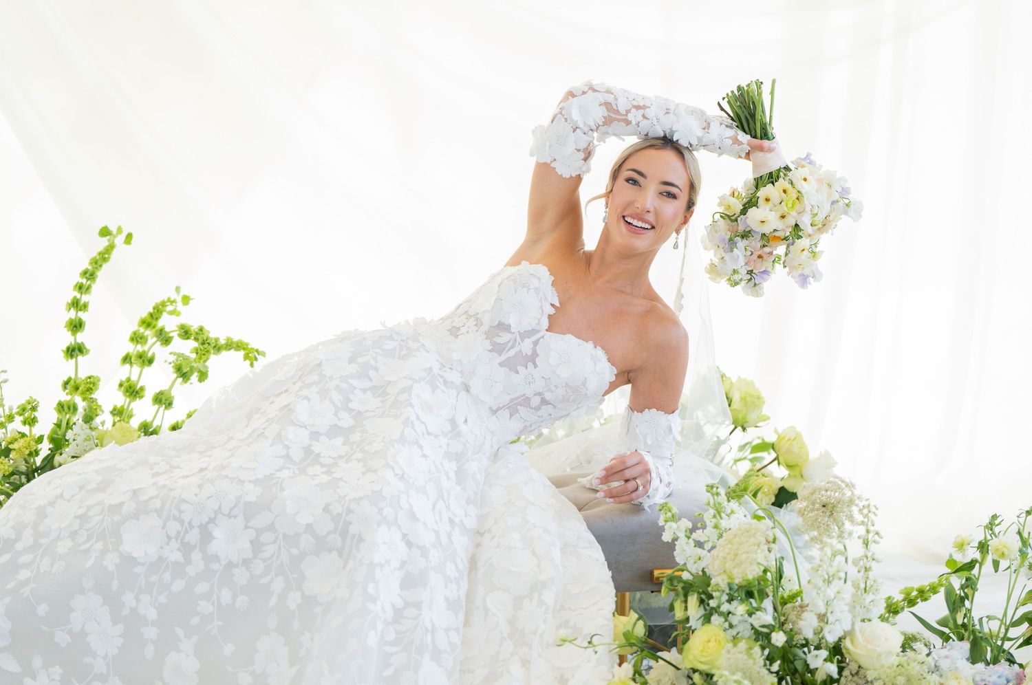 Bride in flowing white dress twirls with bouquet surrounded by green vines and natural light.