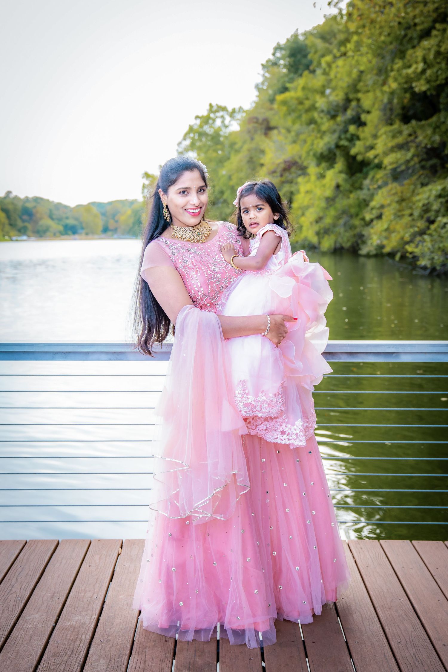 Mother and daughter wearing matching pink tulle dresses on lakeside deck.
