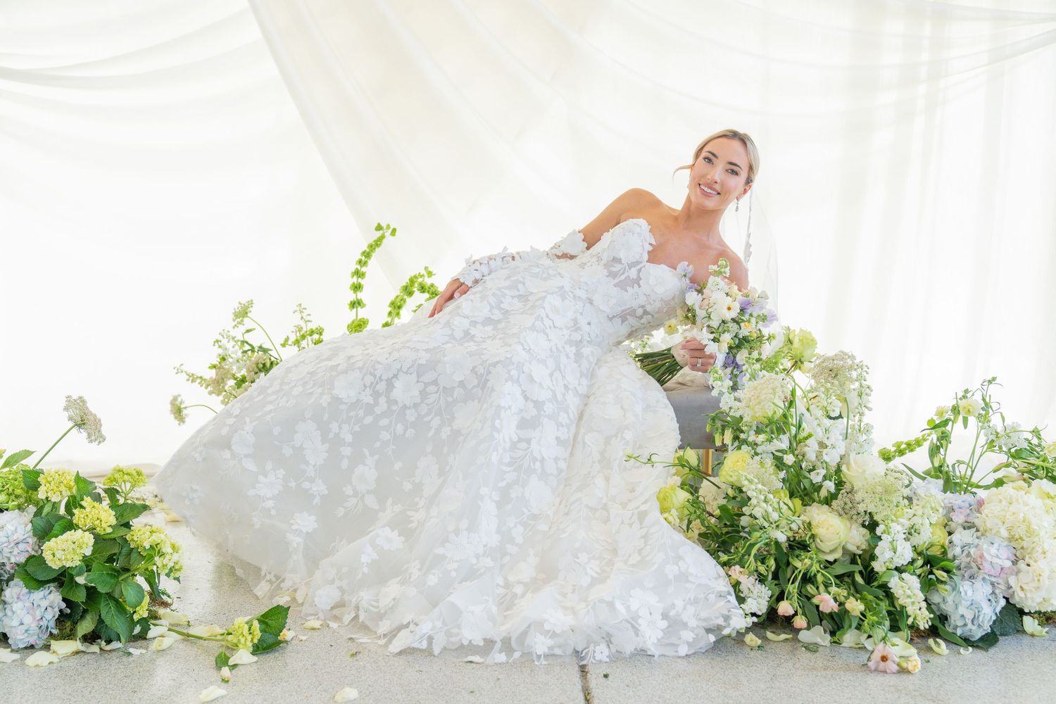 Elegant bridal portrait with white floral bouquet and lace wedding gown against light background.