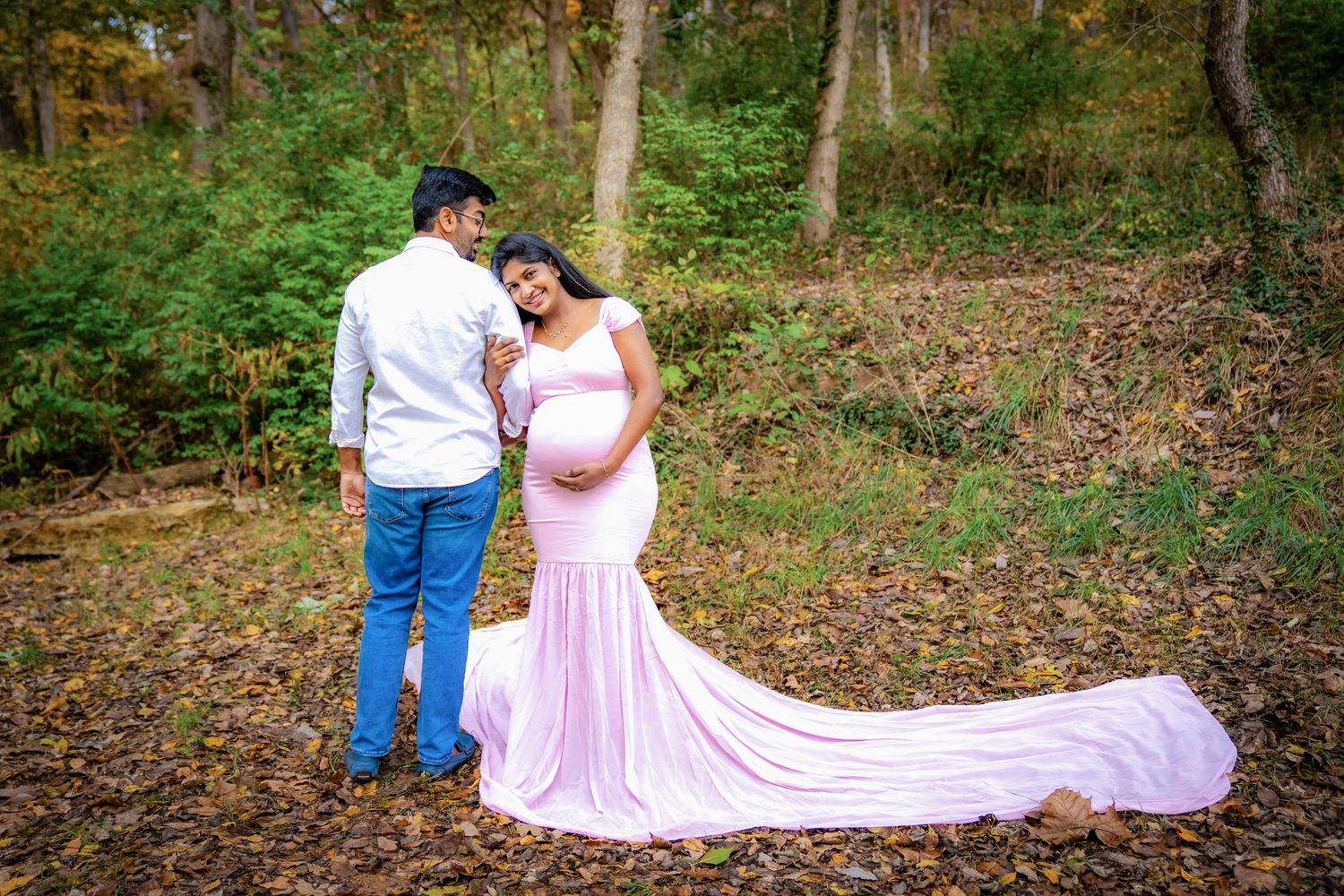 A couple shares a tender moment in a wooded setting with a flowing pink dress.