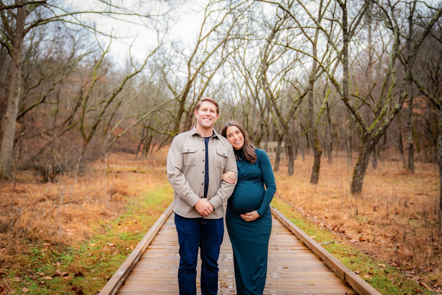 Couple walking along a wooden path surrounded by bare winter trees.