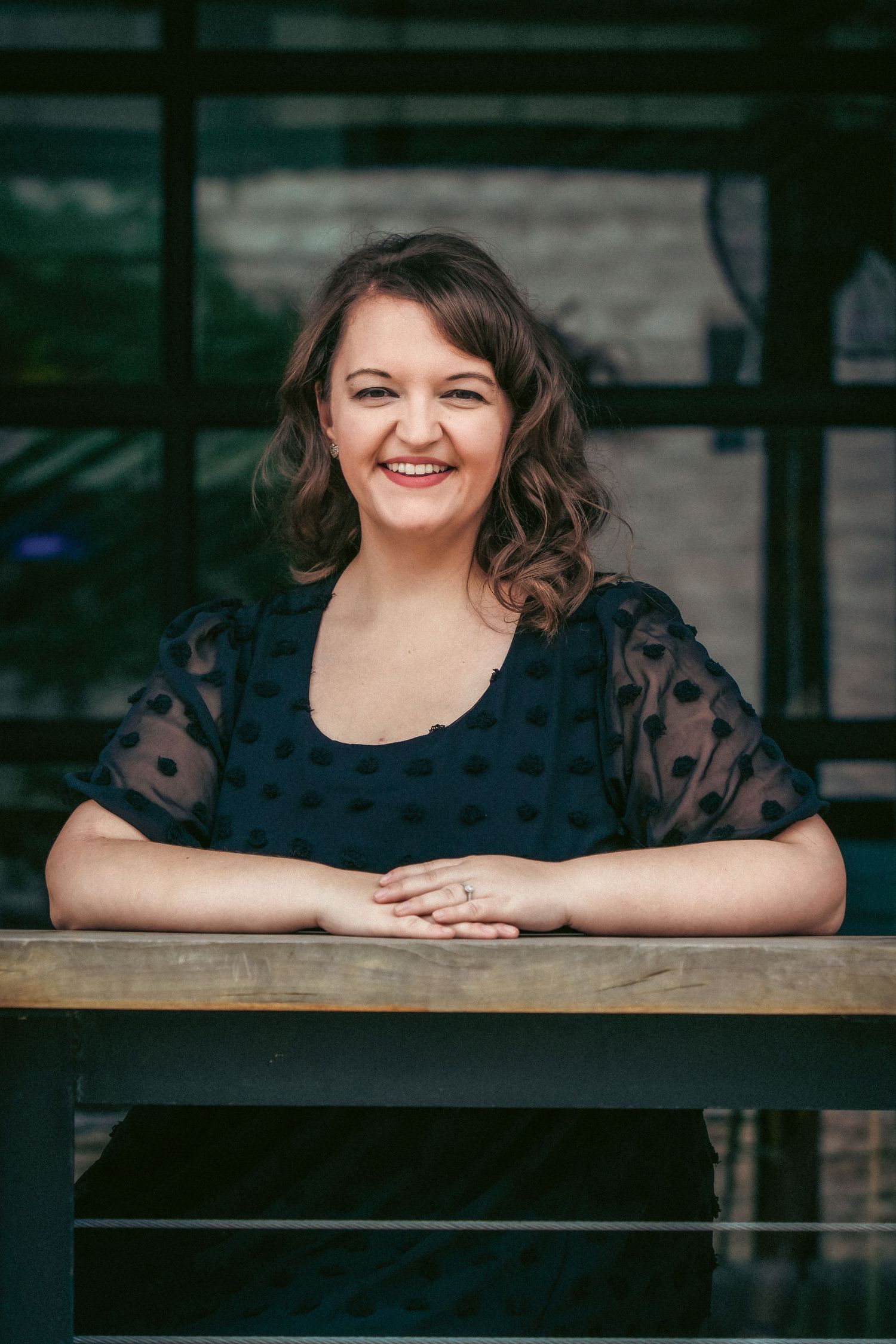 A person in a black polka dot dress poses against a dark wooden backdrop.