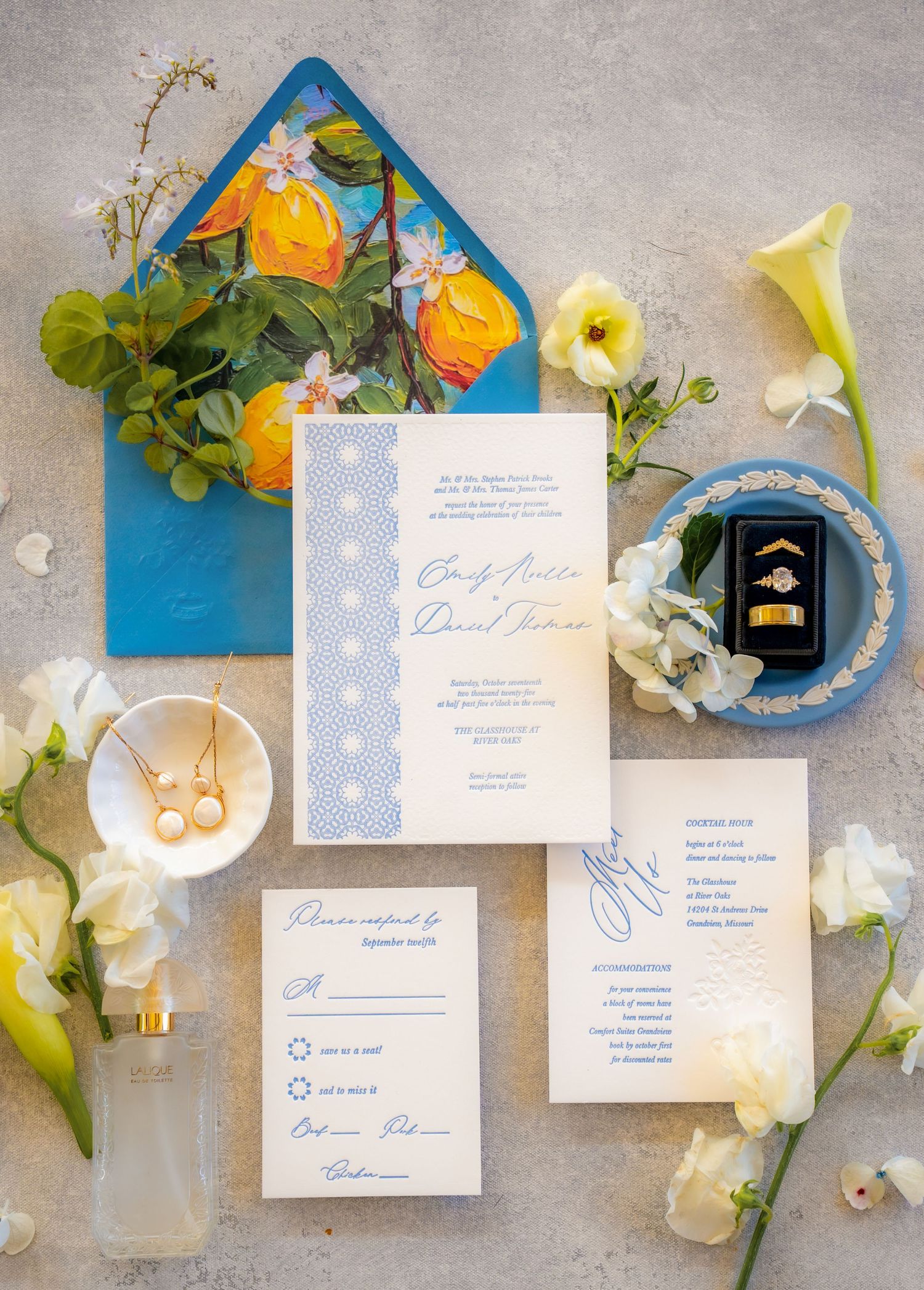 Elegant wedding invitation suite with blue envelope, calla lilies, and delicate floral accents on a gray background.