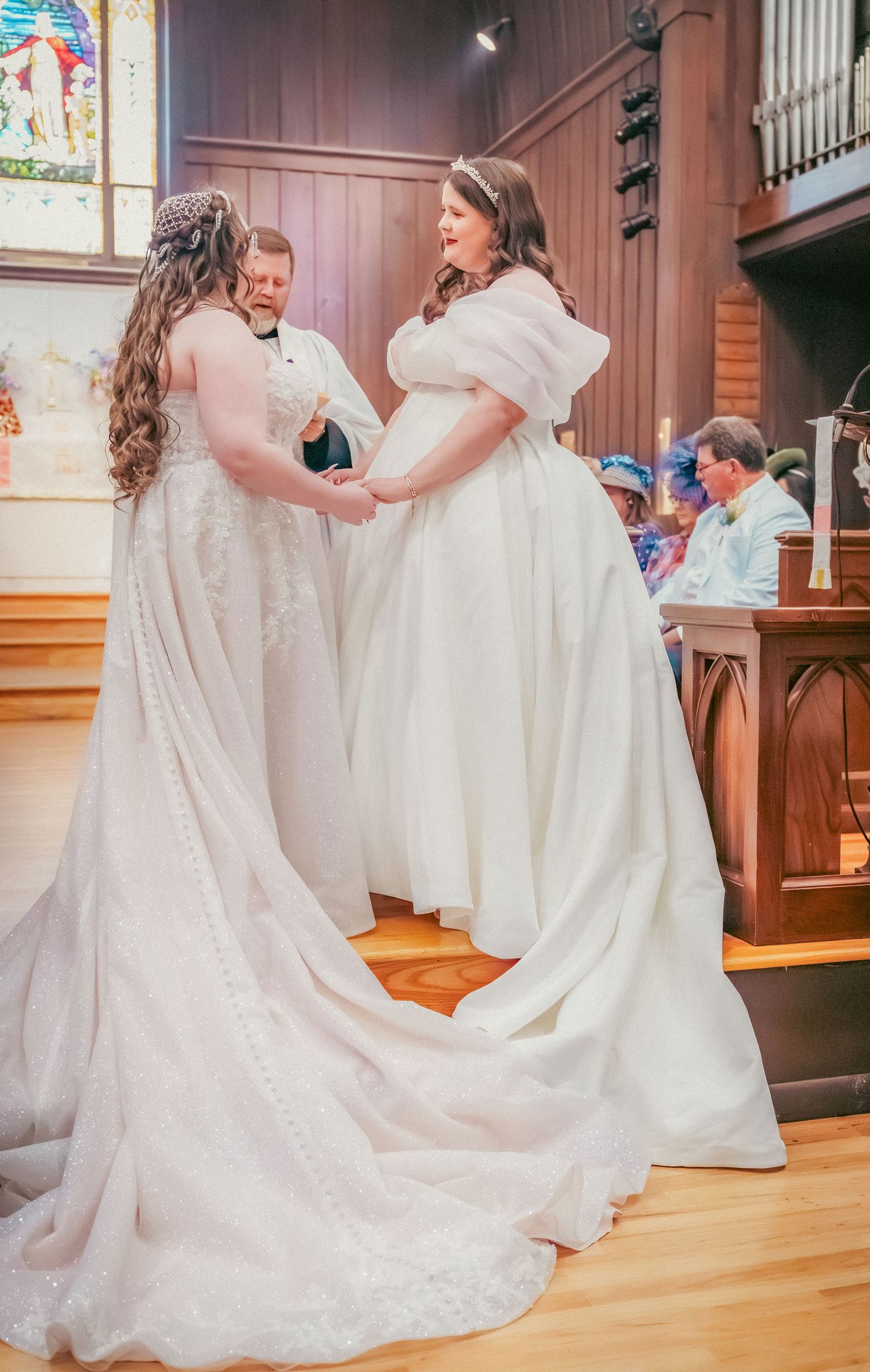 Two people in white wedding gowns share a joyful moment together in a church setting.