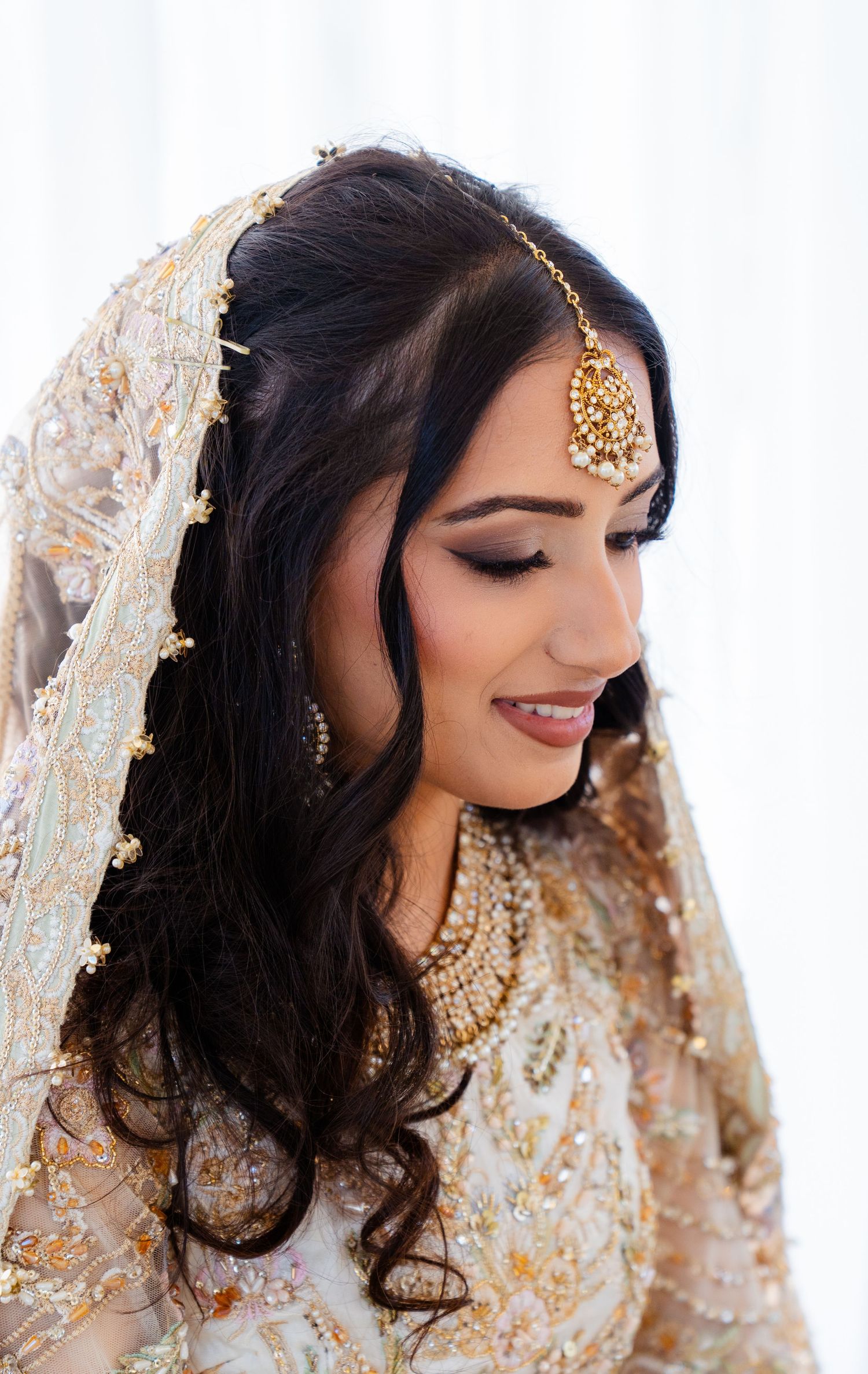 Elegant South Asian bride wearing cream and gold lehenga with ornate jewelry and veil.