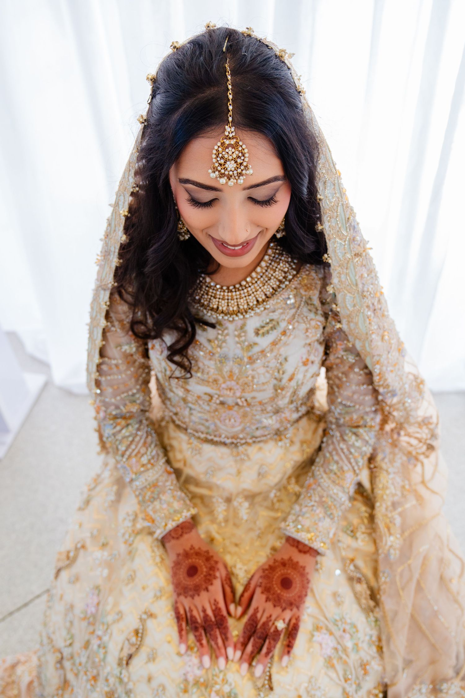 Bride in cream and gold attire showing traditional mehndi designs on hands.