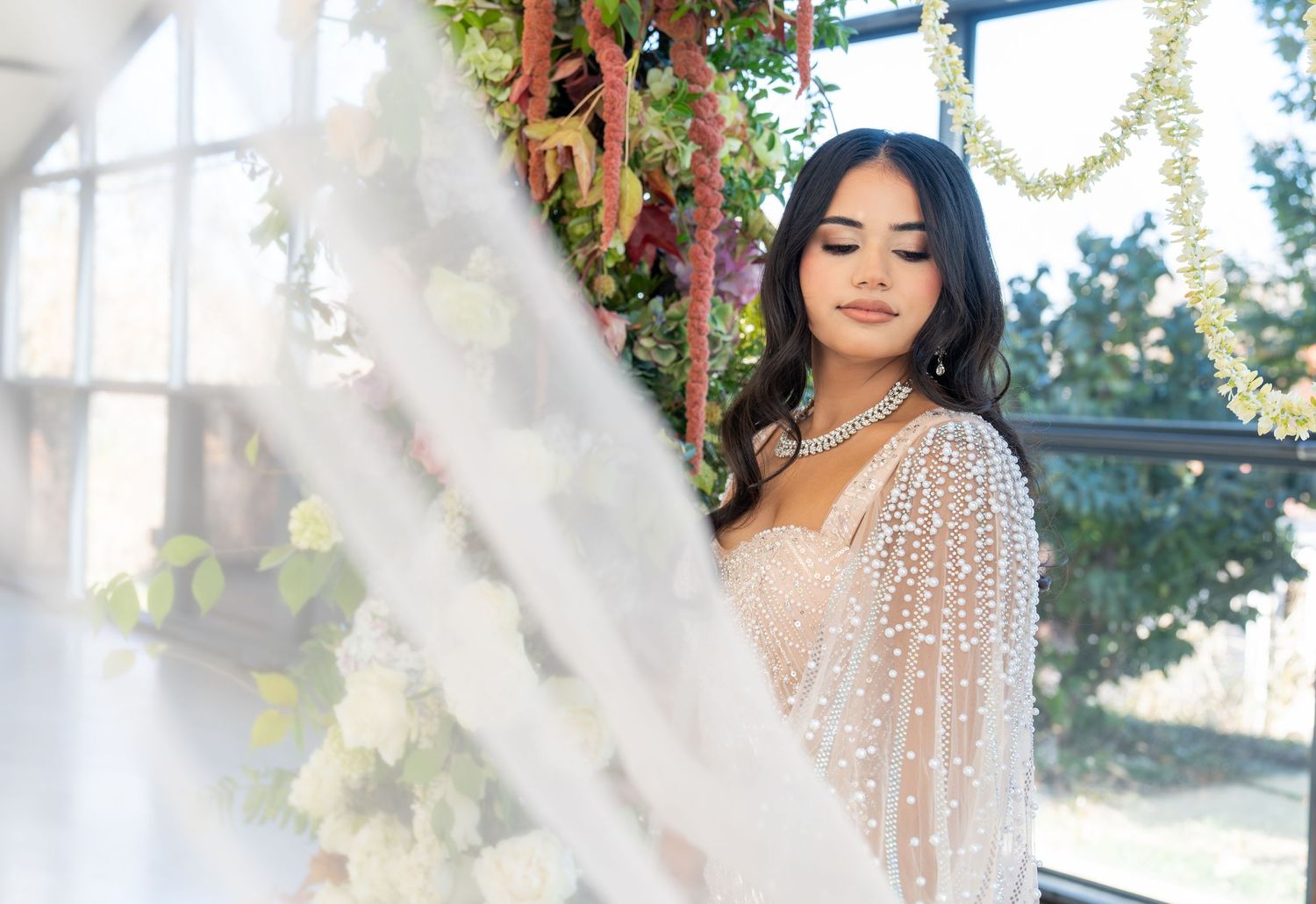 A dreamy bridal portrait in a conservatory with natural light streaming through windows and floral decorations.