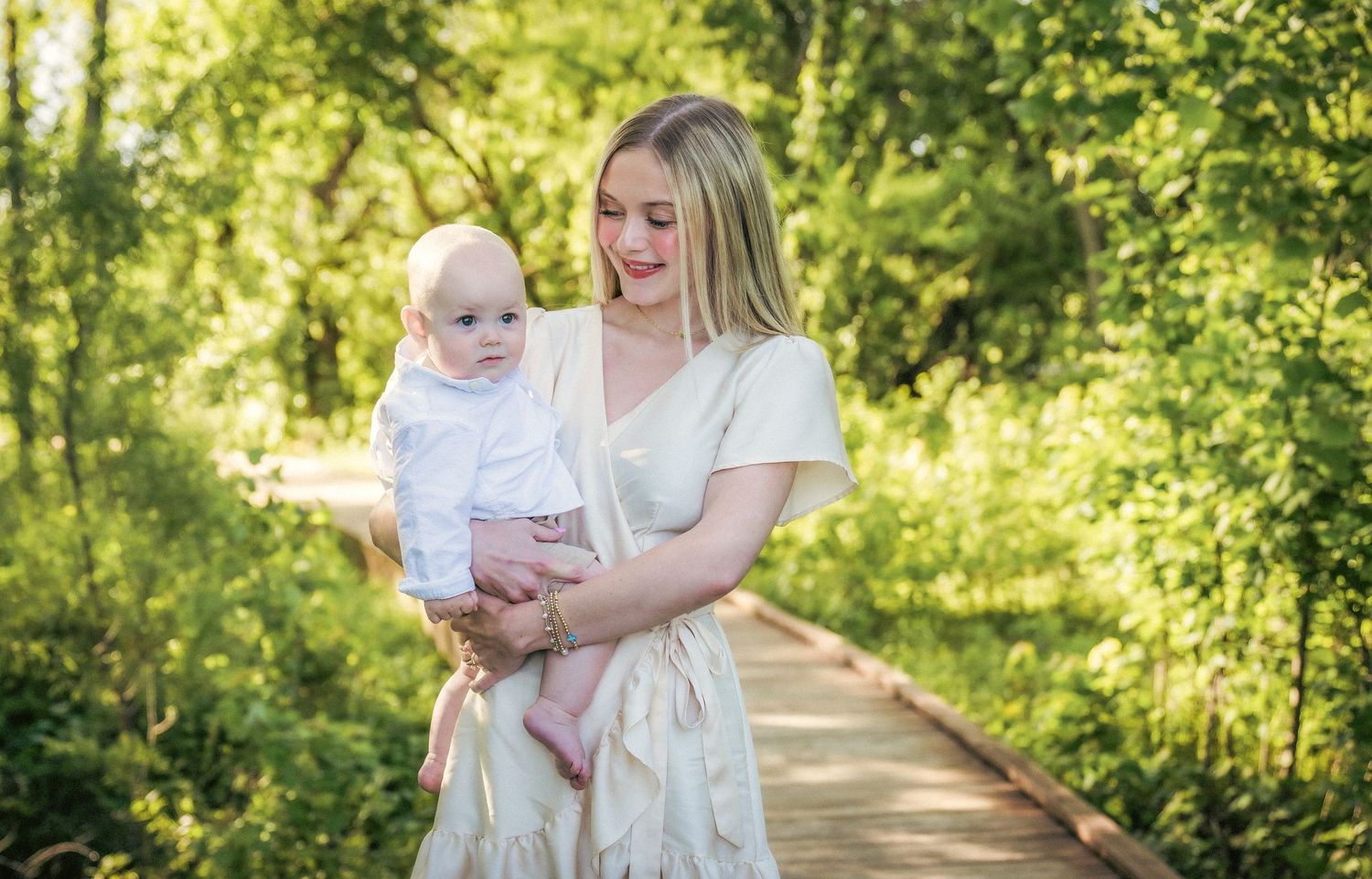 Mother and child walking hand in hand down sunny nature path in summer dresses.