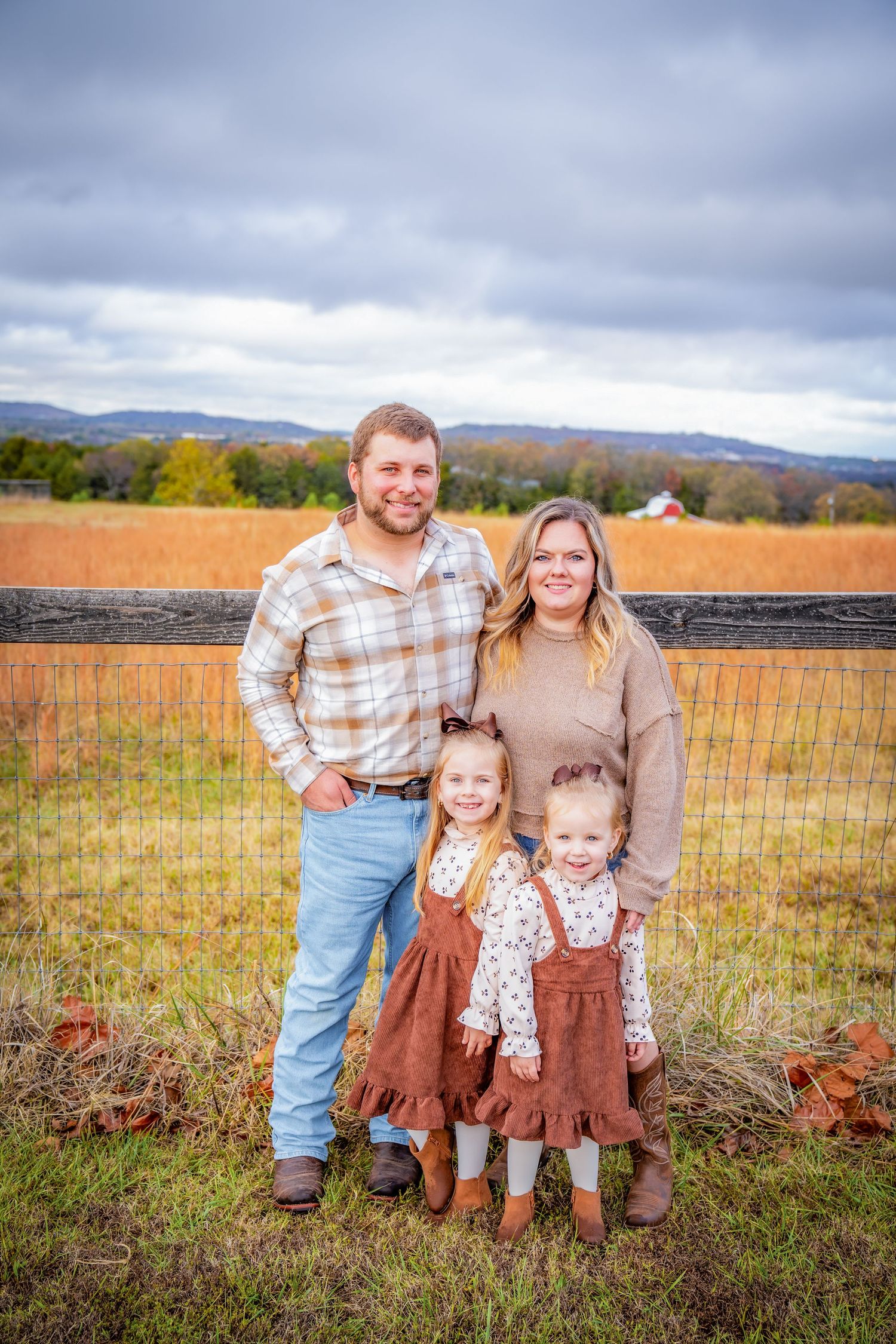 Family portrait in casual attire against fall foliage and cloudy mountain backdrop.