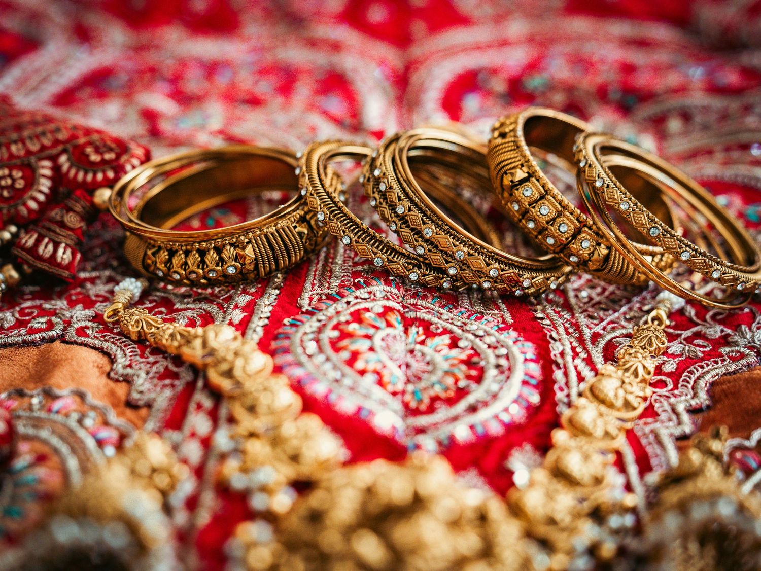 Close-up details of traditional Indian gold jewelry and red embroidered fabric with intricate patterns.