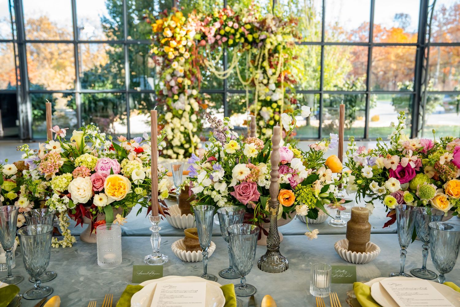 Wedding reception table decorated with glass vases, flowers and candles under a floral arch.