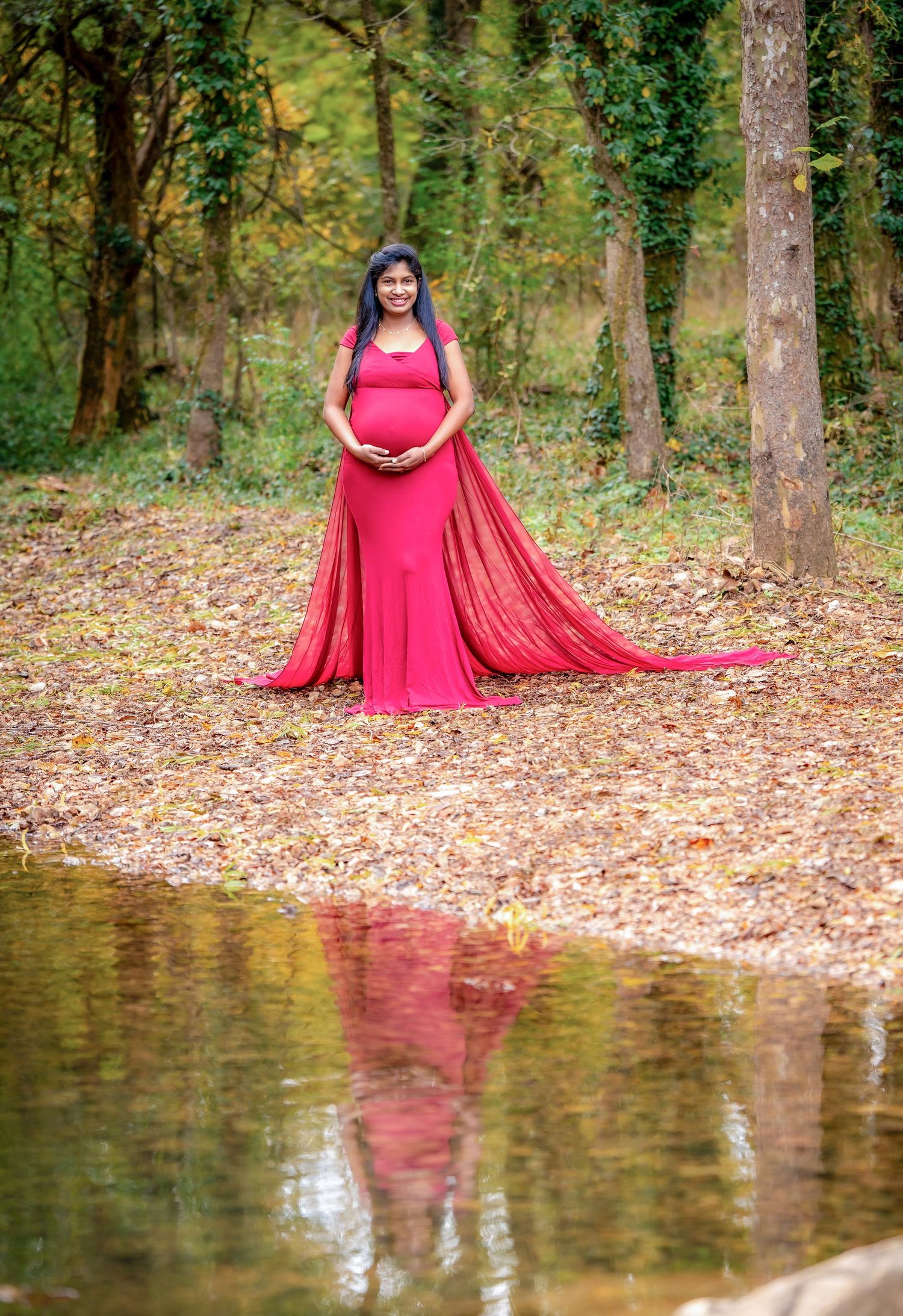 Red dress creates beautiful reflection in pond water surrounded by fallen autumn leaves.