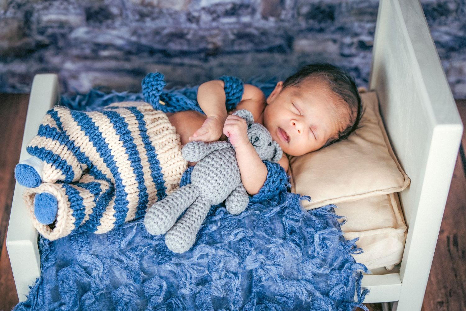 Newborn baby sleeping peacefully on blue textured blanket with striped accessories.