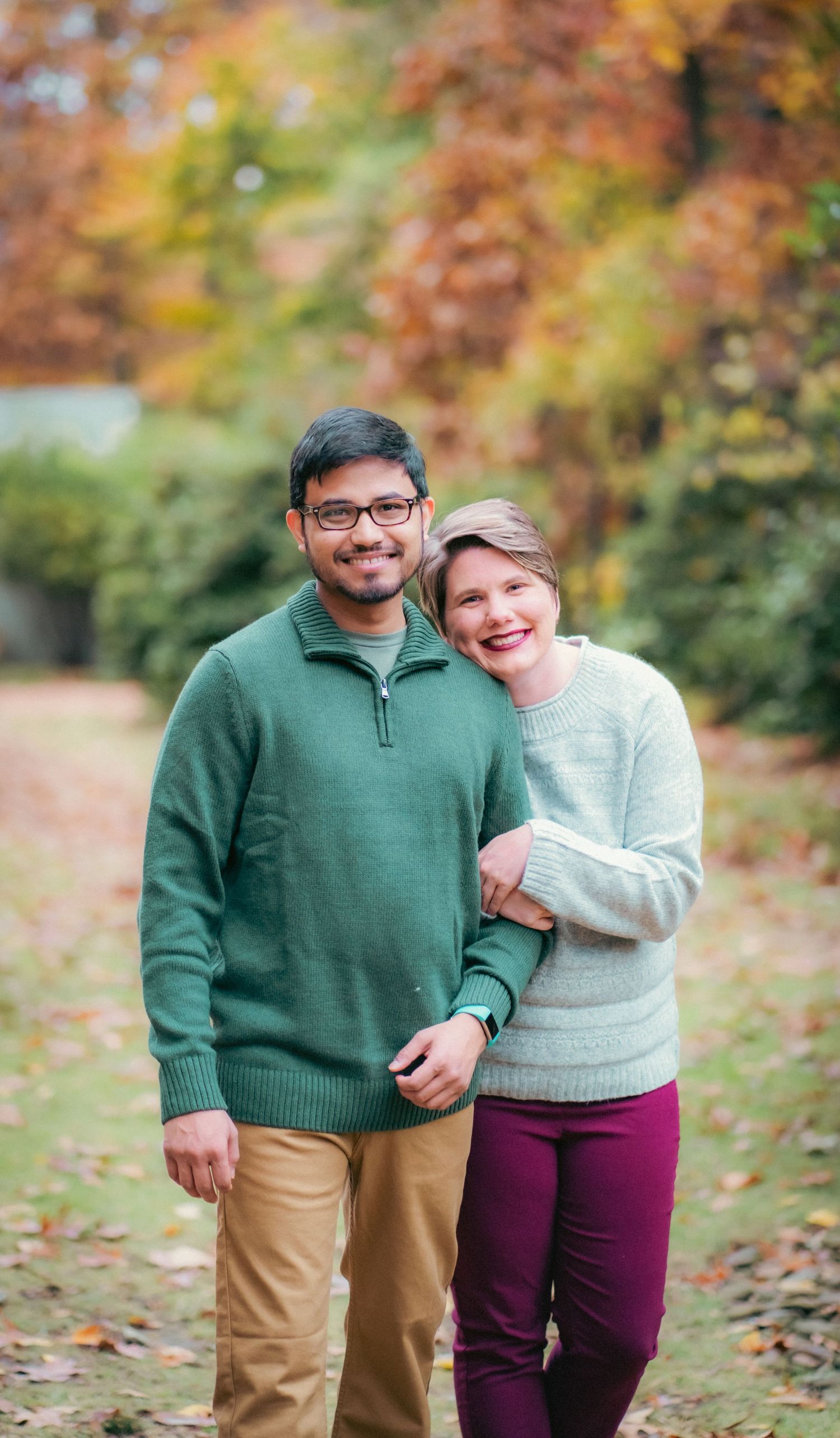 Couple wearing green and beige sweaters posing together on autumn leaves.