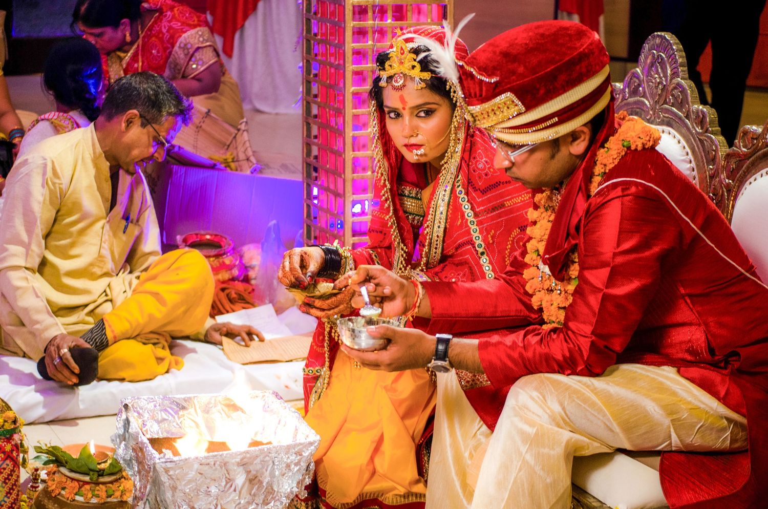 Traditional Indian wedding ceremony with vibrant red and gold decorations and rituals being performed.