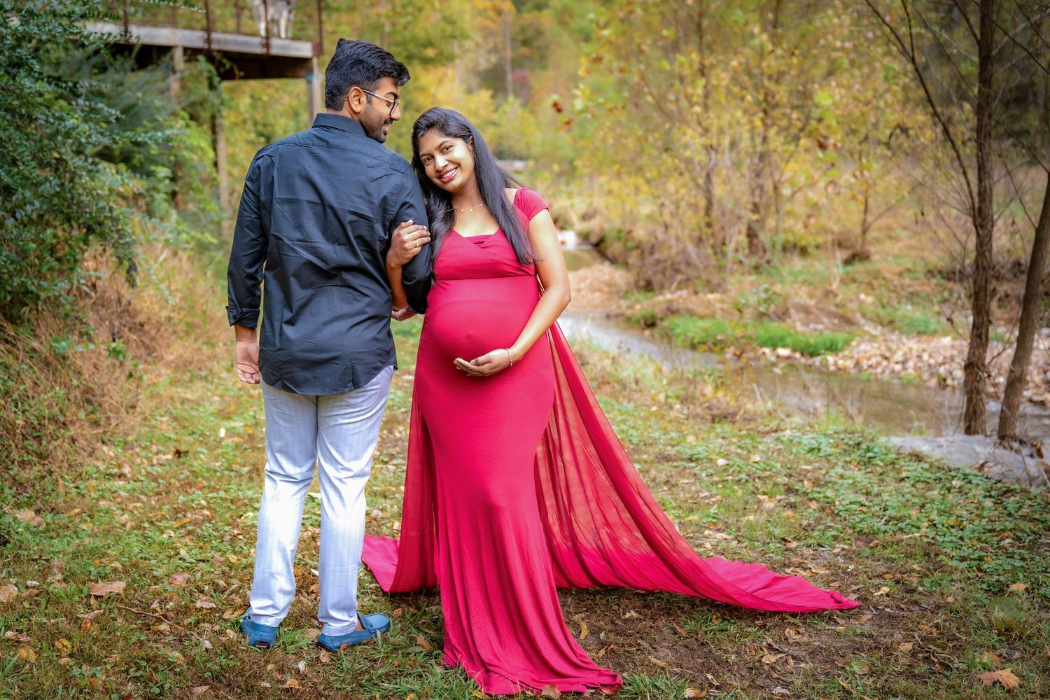 A couple poses together in a natural setting with autumn foliage and fallen leaves.