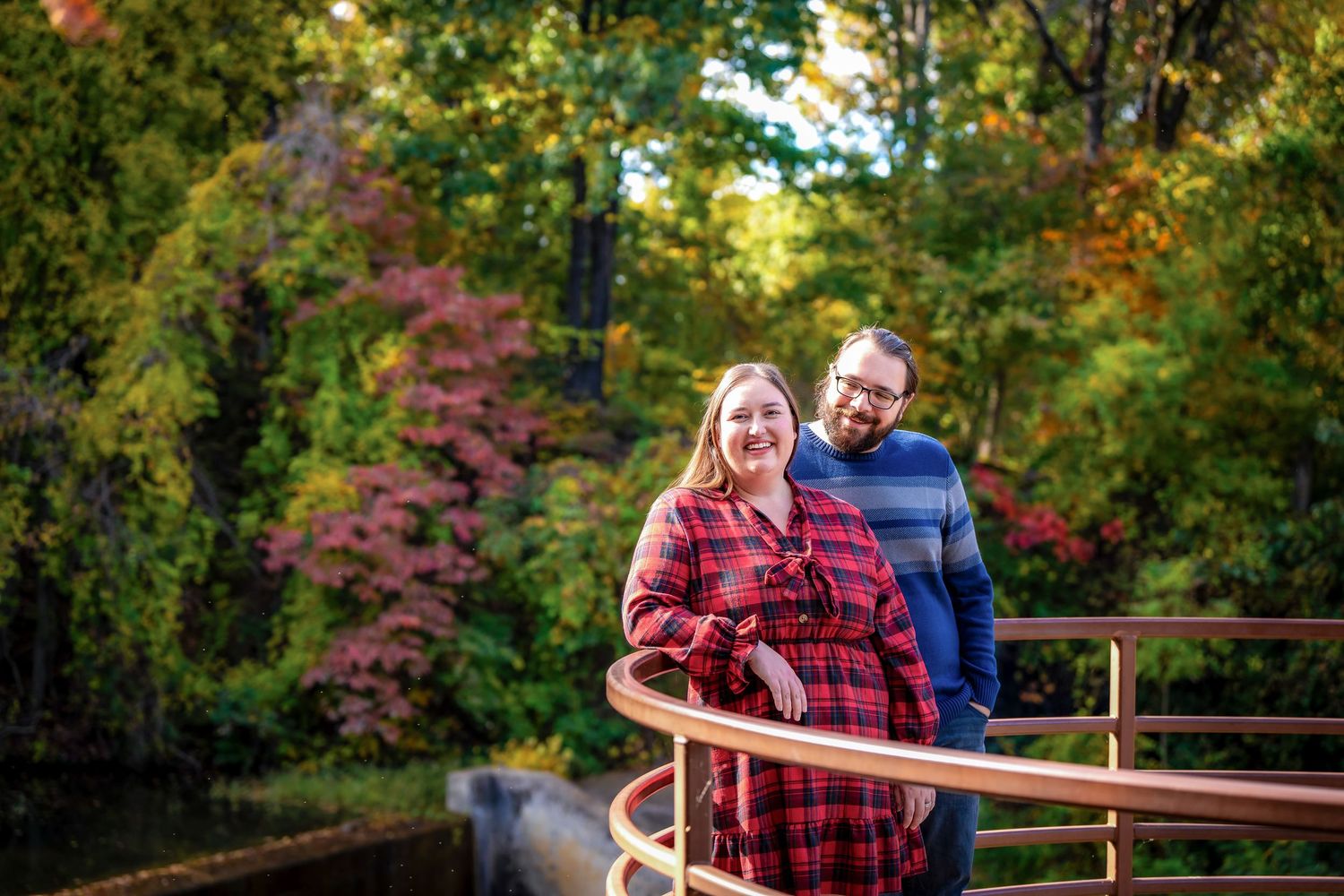 Autumn engagement photos of couple on rustic wooden bridge with fall foliage.