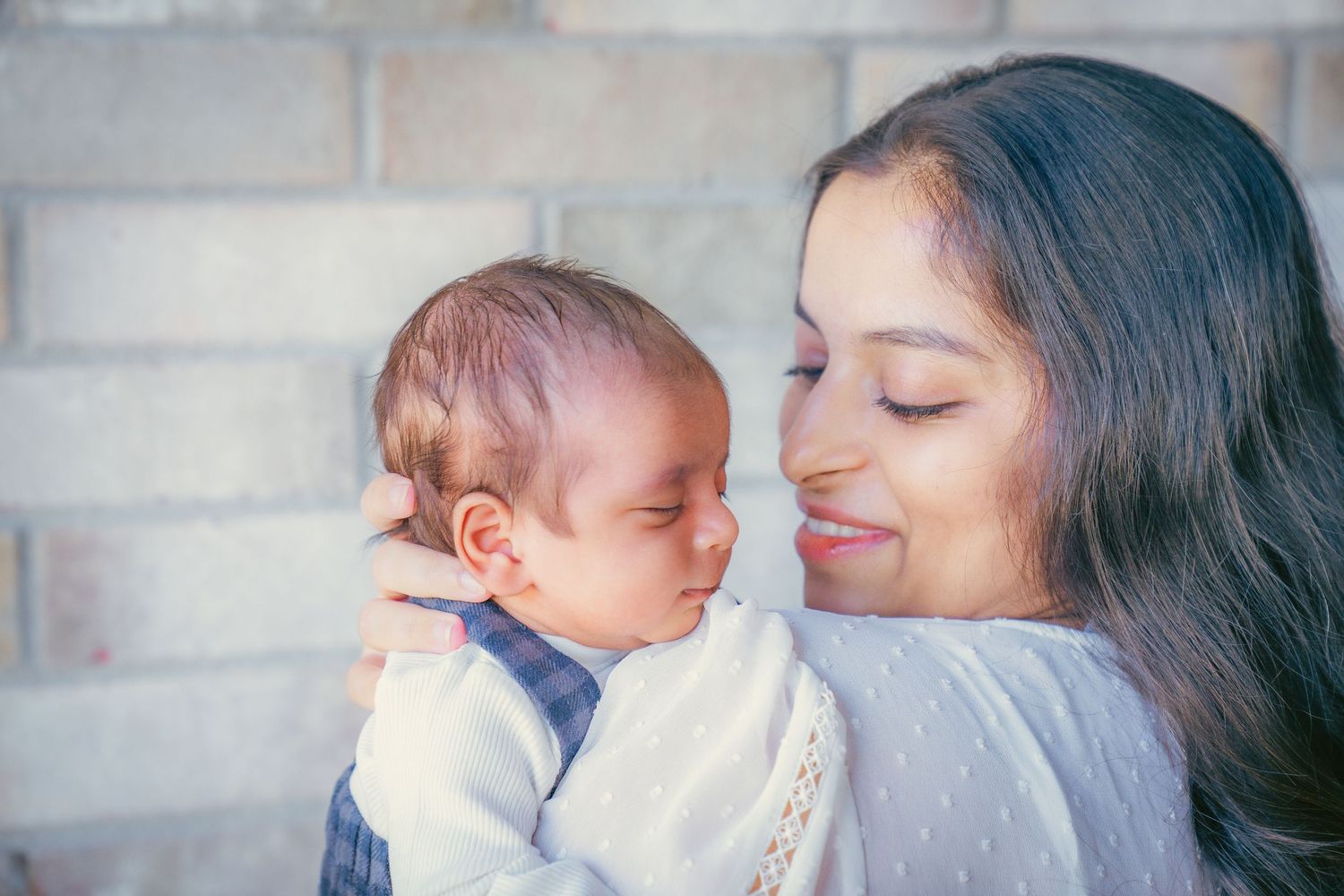 Tender moment captured between parent and baby against white brick wall.