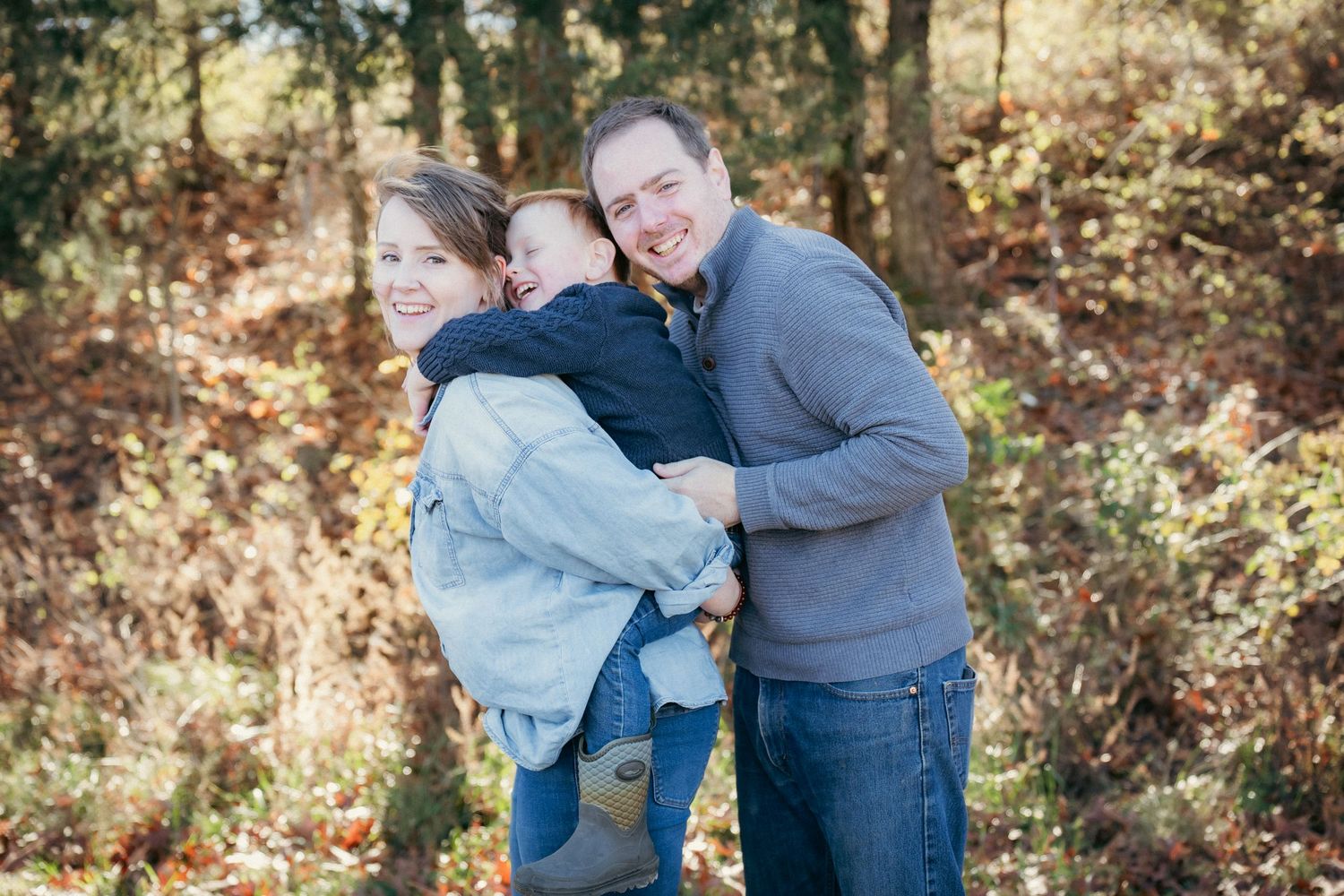 Family playing and laughing together in wooded area with fall foliage.