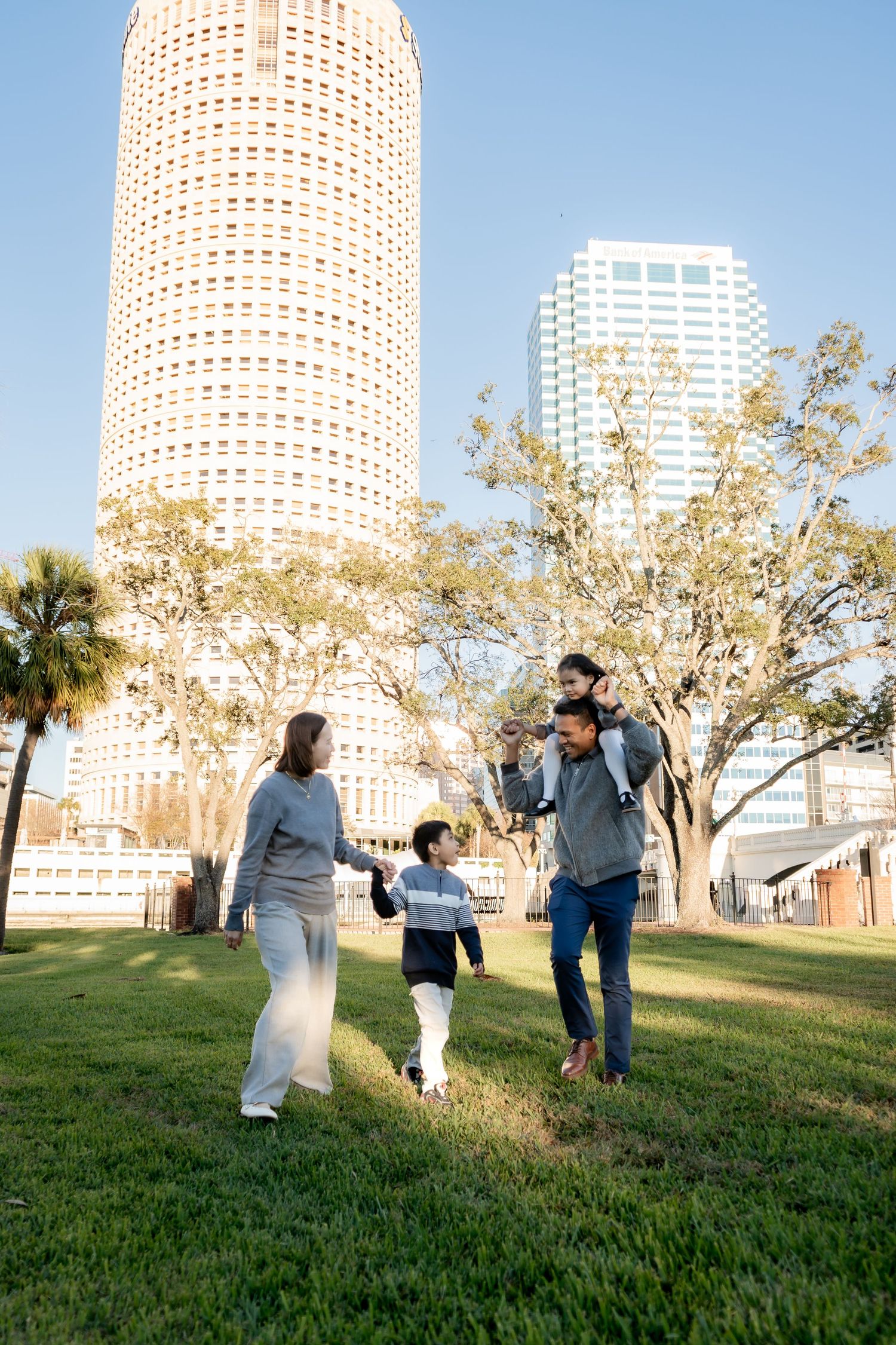 Family of four enjoying a sunny day in an urban park with a tall skyscraper in the background.