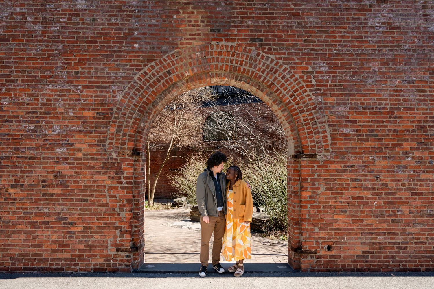 Couple sharing a romantic moment under a red brick archway in an outdoor garden setting.