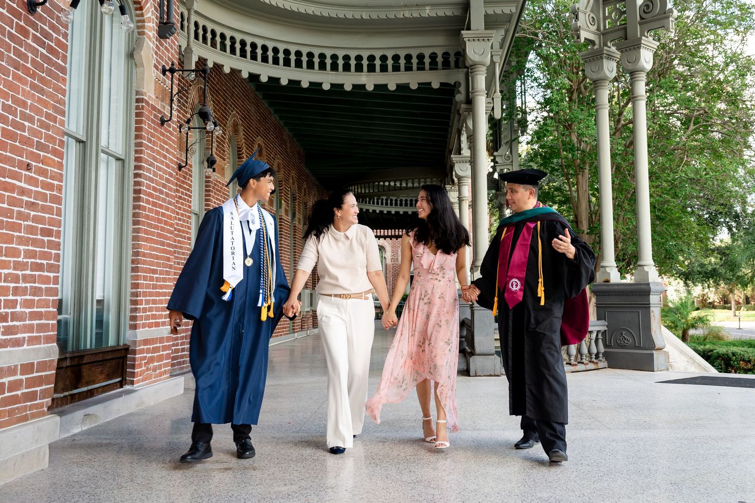 Four people in graduation attire walk together on a university campus colonnade celebrating commencement day.