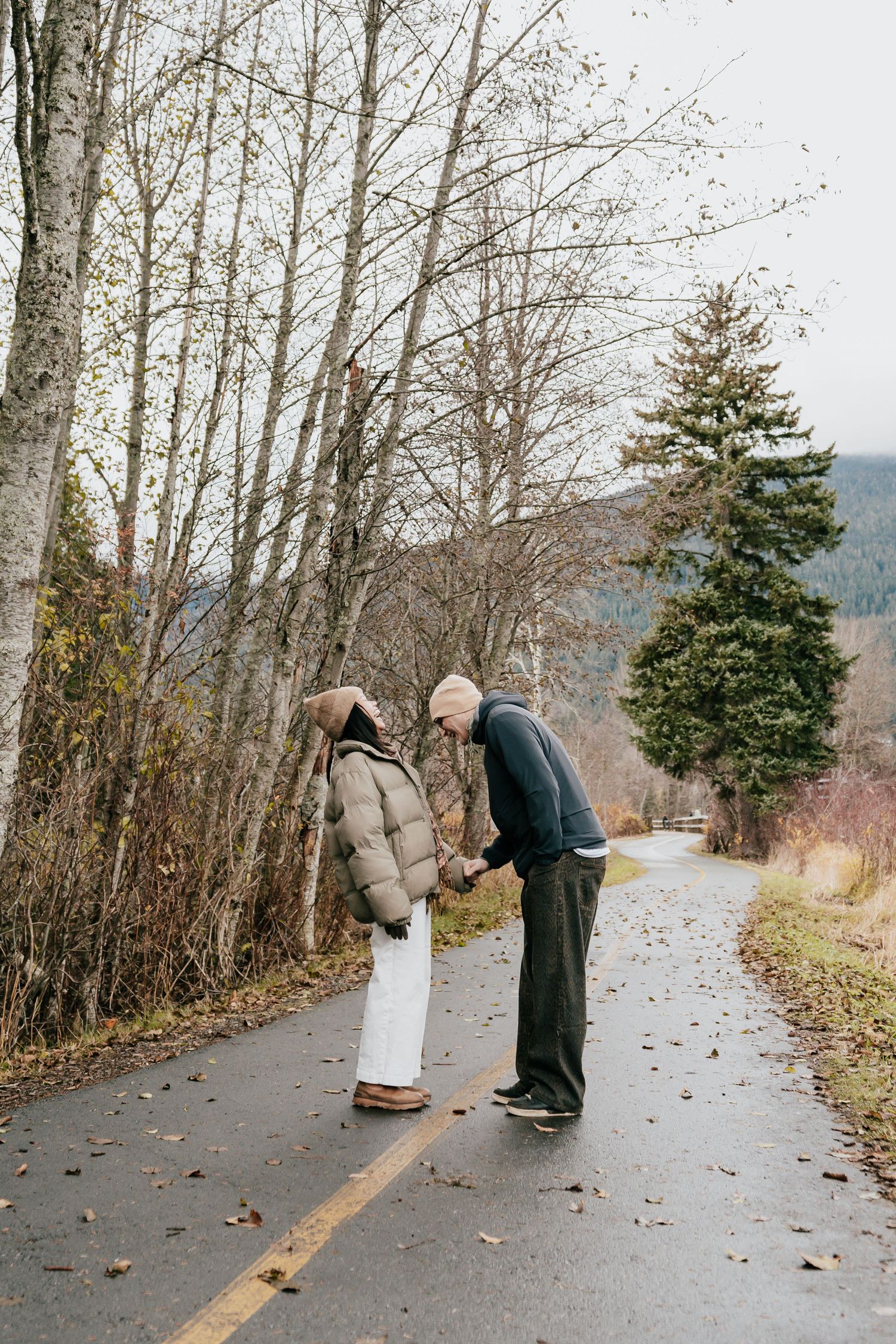 Couple holding hands and bowing to each other on a quiet road surrounded by bare autumn trees.
