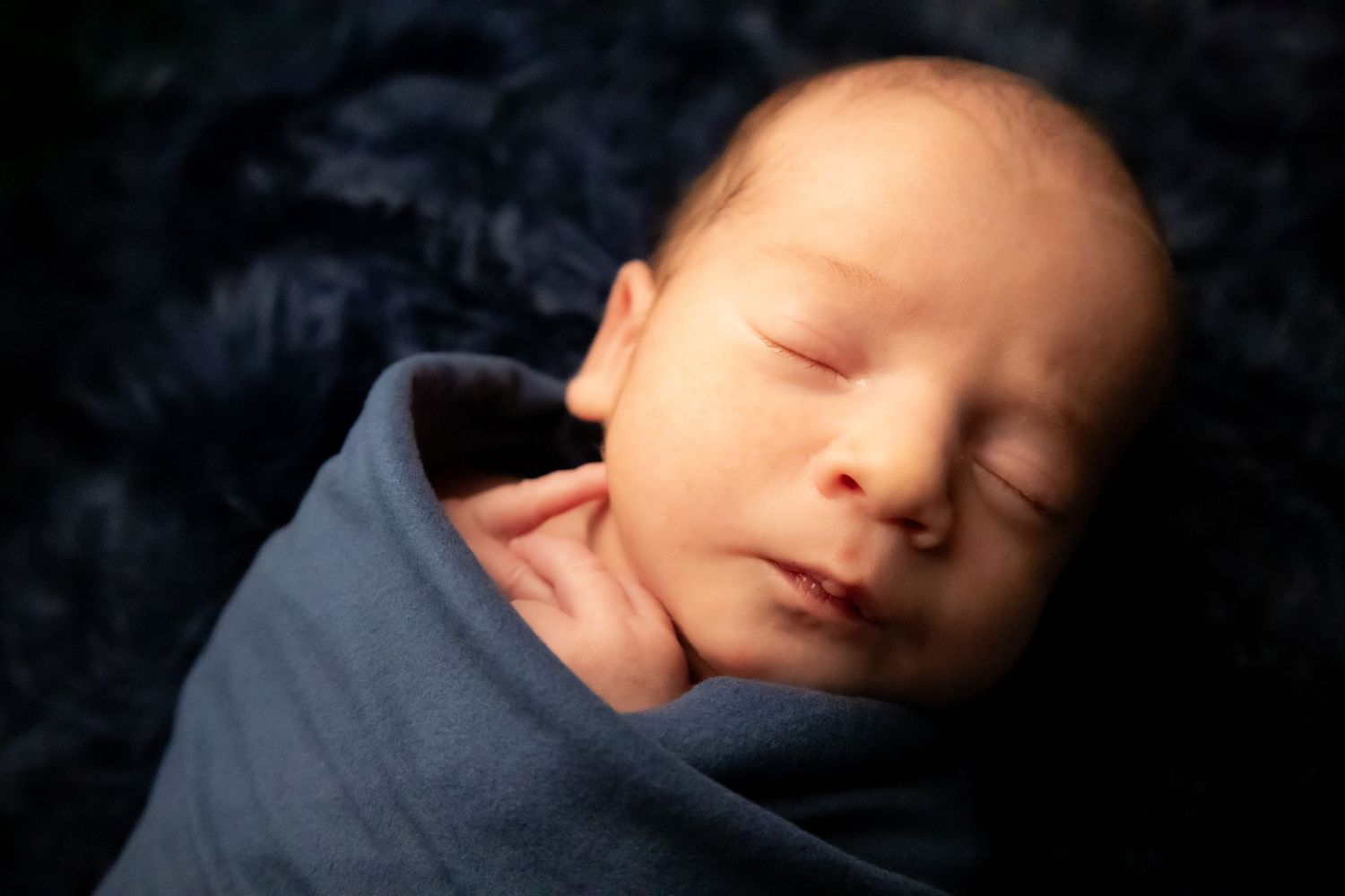 Newborn in a navy blue wrap sleeping with his hand peeking out of the top of the wrap
