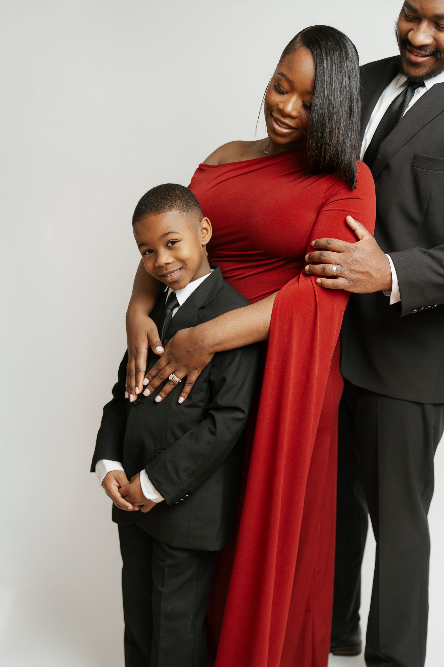 A family in coordinating red and black formal attire poses together in a studio against a white backdrop.