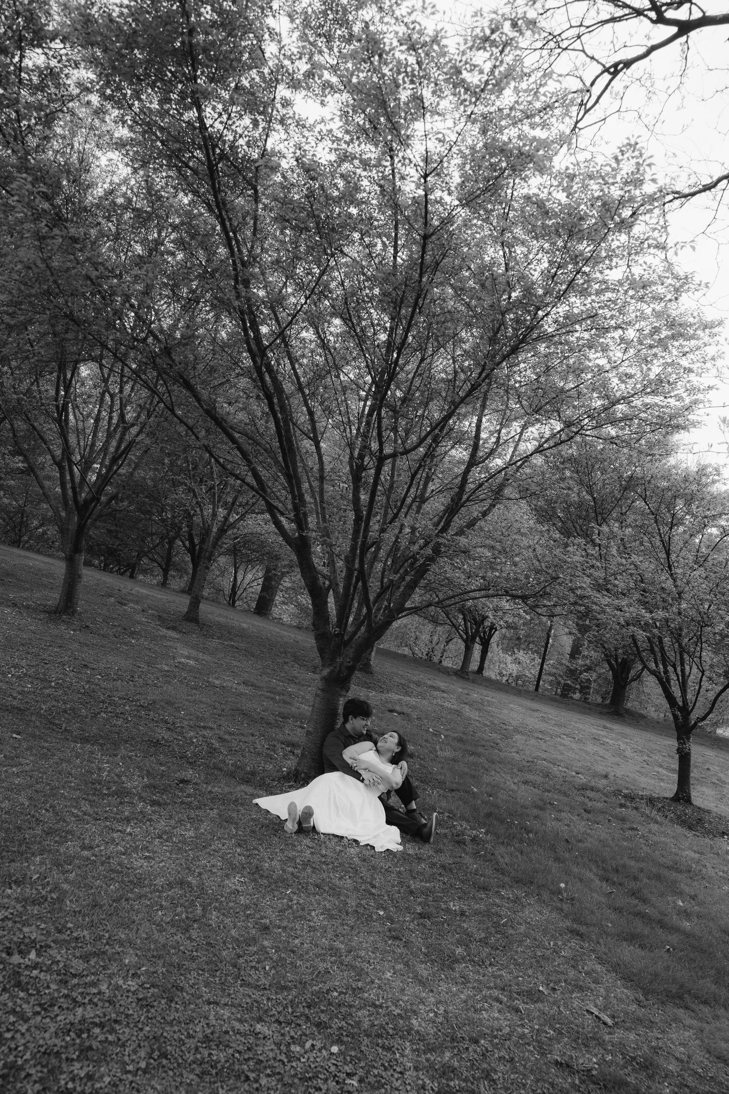 Black and white photo series of a couple relaxing on a grassy hillside under trees.