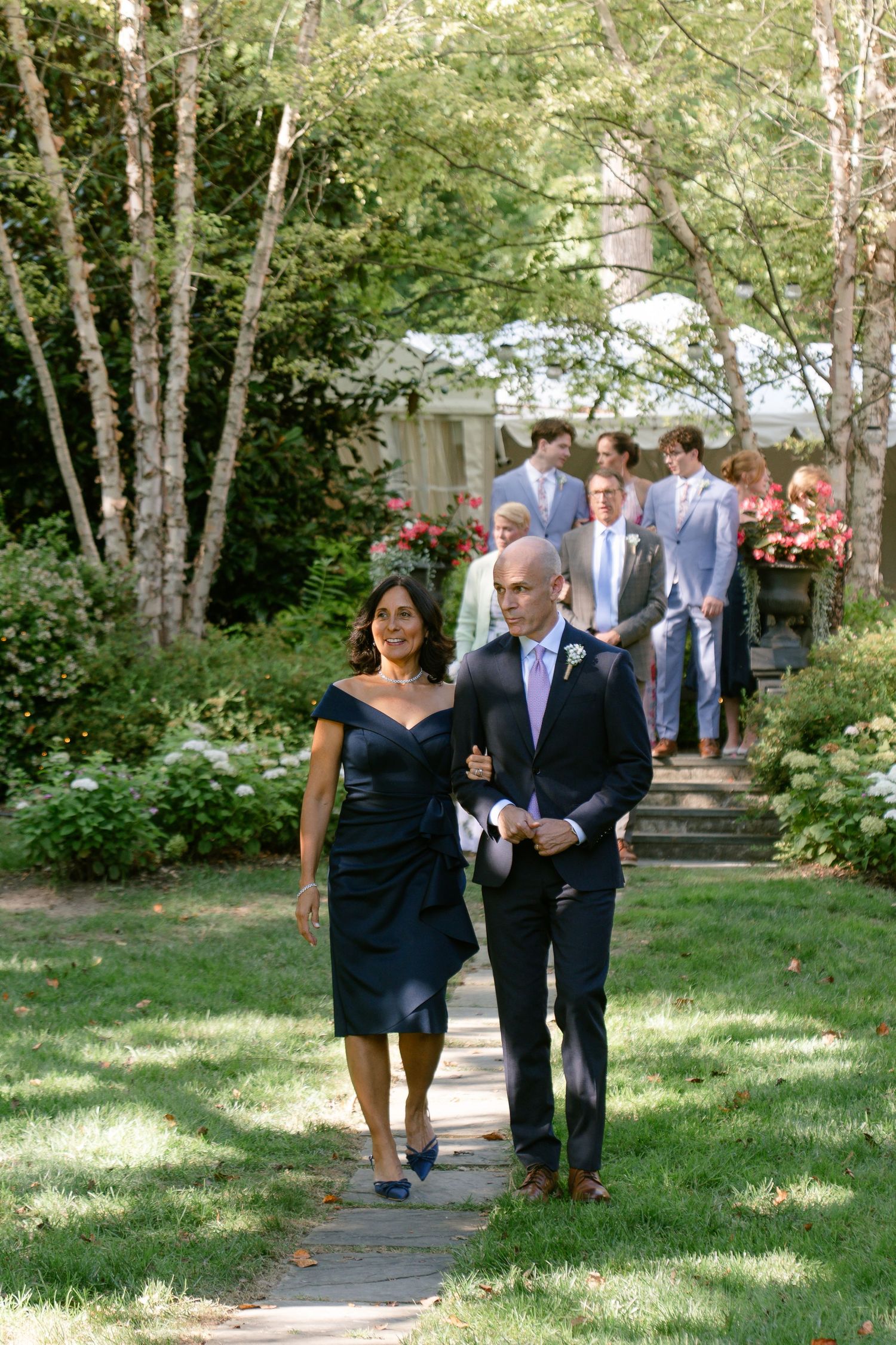 Wedding guests walking along garden path lined with birch trees.