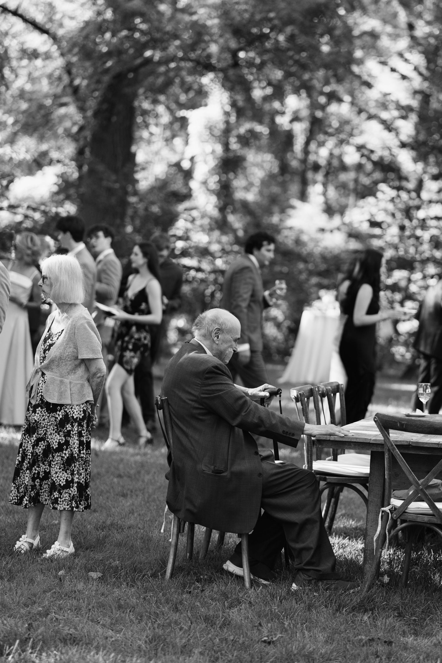 Wedding guests relax in chairs during outdoor garden reception in black and white.