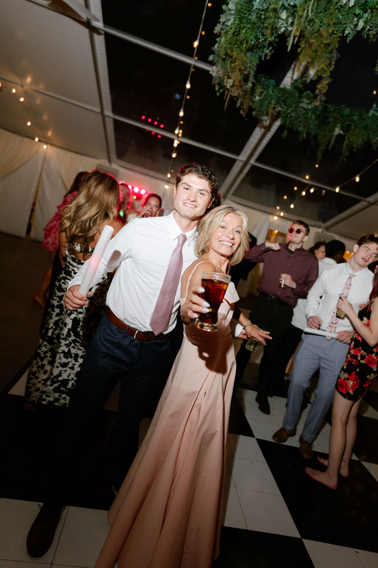 Wedding guests dancing and celebrating on a checkered dance floor under string lights.