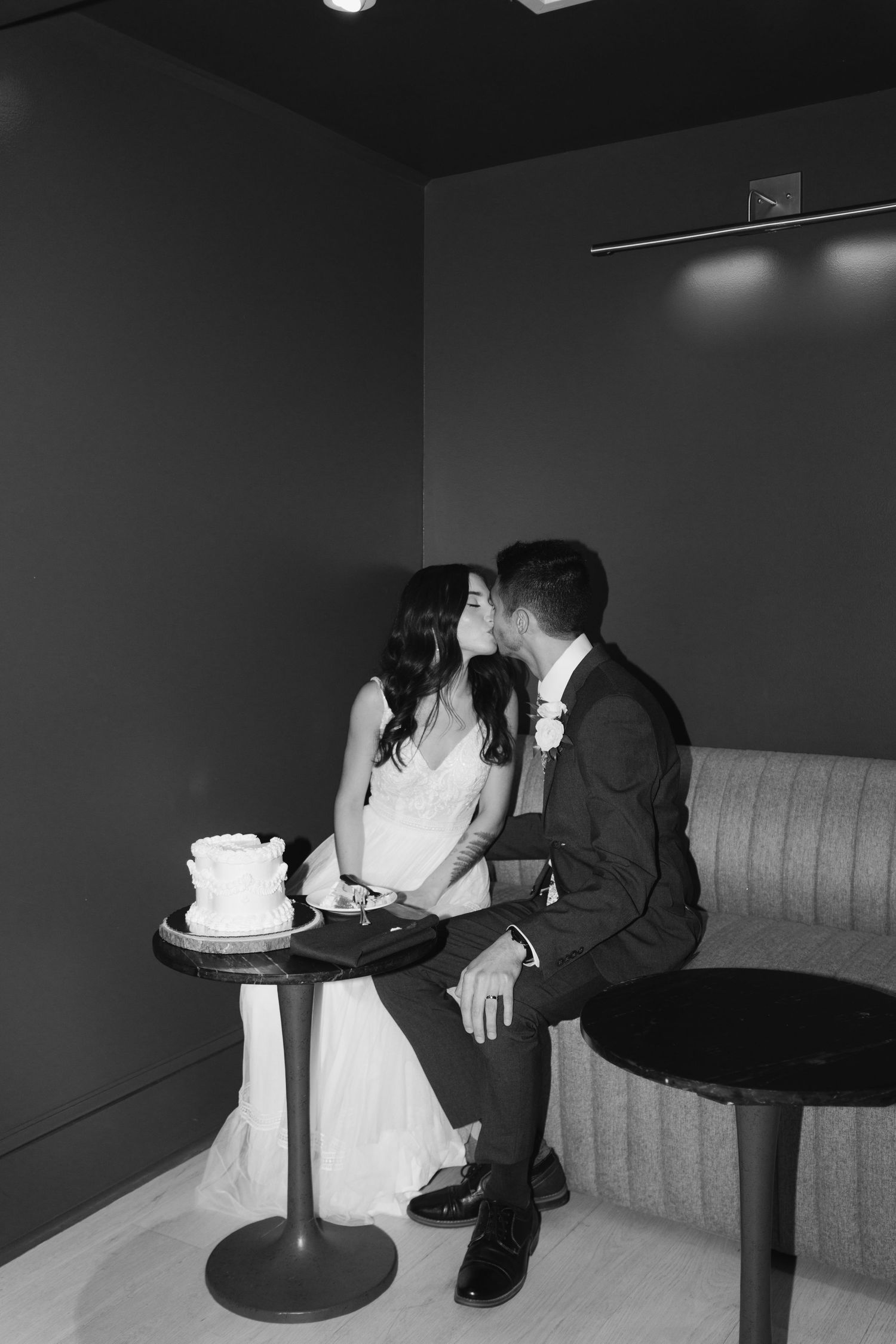 A black and white photo of a couple sharing an intimate moment at a small table with a cake.