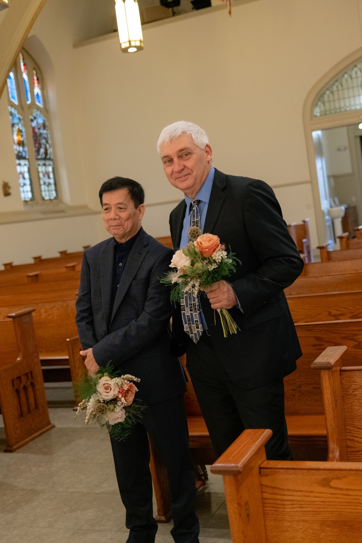 Men in black suits share a lighthearted moment in wooden church pews.