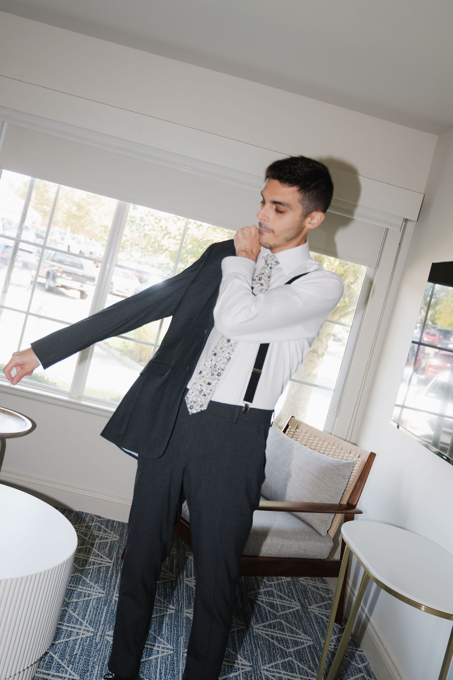 A person in a black suit performs a dramatic dance move while leaning back in a bright white room.