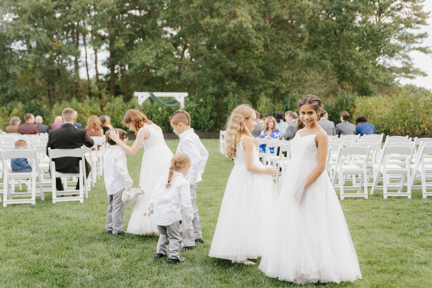 A joyful wedding celebration with guests seated outdoors in white chairs during a sunny afternoon ceremony.