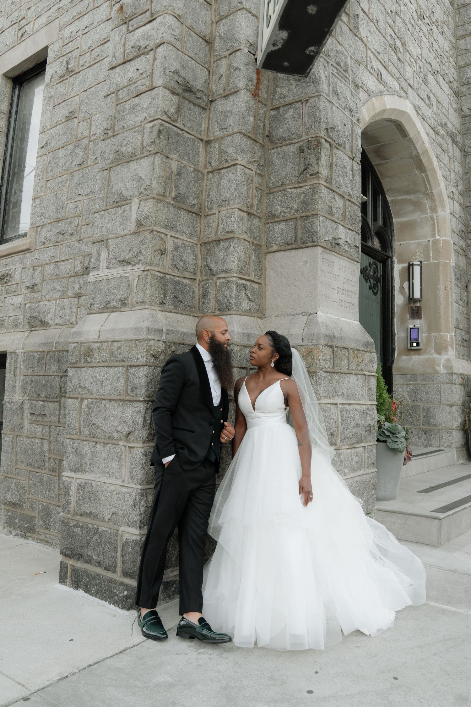 Wedding couple sits together on stone steps of historic building in romantic poses.
