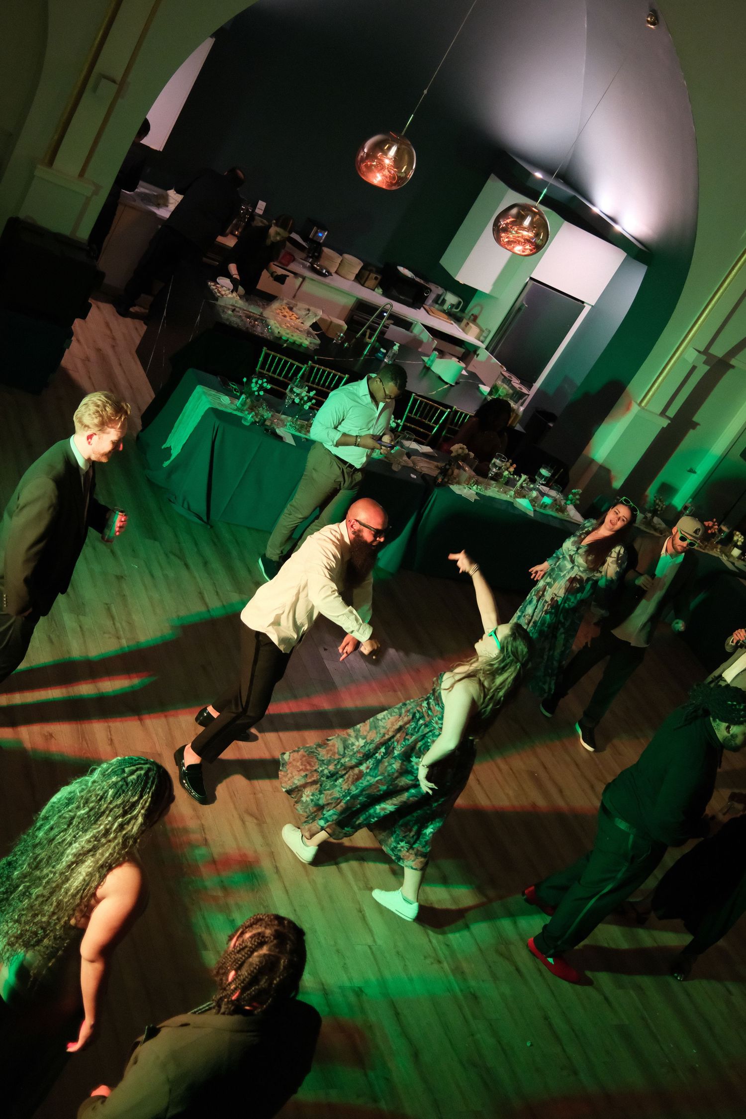 Dance floor illuminated with green lighting as guests dance at wedding reception.