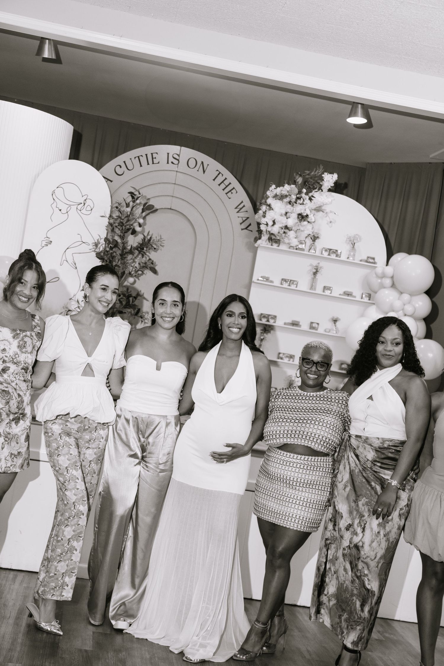 A group photo session with people wearing white outfits against a decorated wall with balloons.
