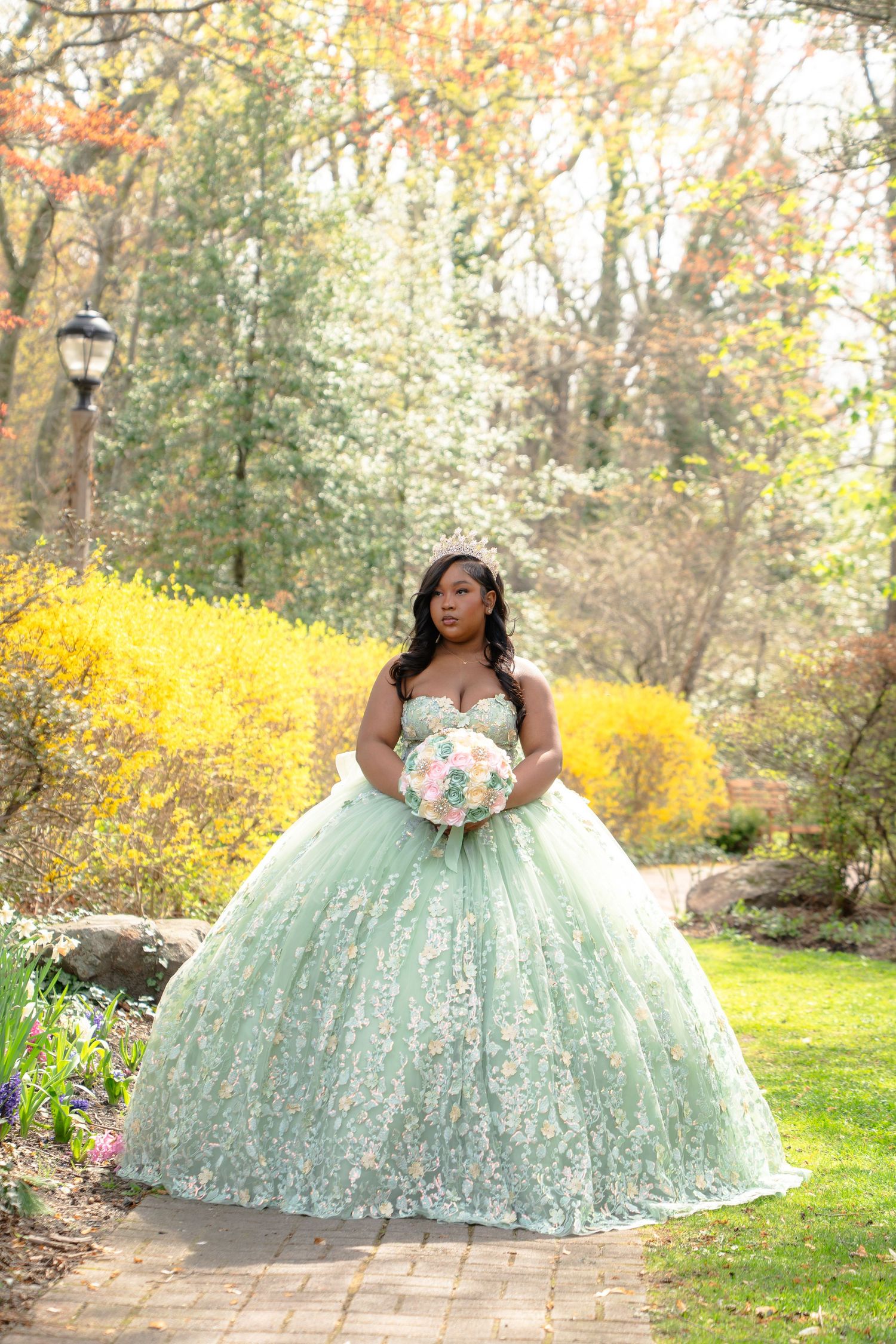 A mint green ballgown dress photographed in a garden setting with blooming yellow forsythia in spring.