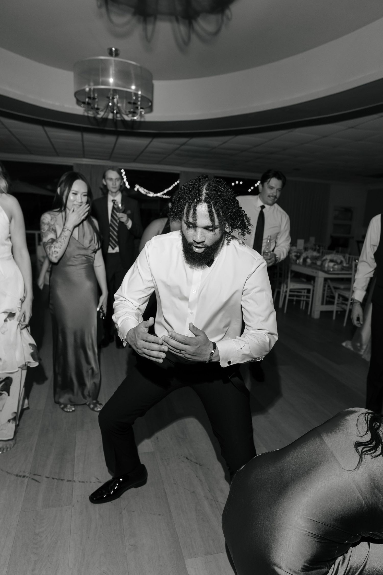 Man in white shirt dancing energetically on wedding reception dance floor in black and white photo.