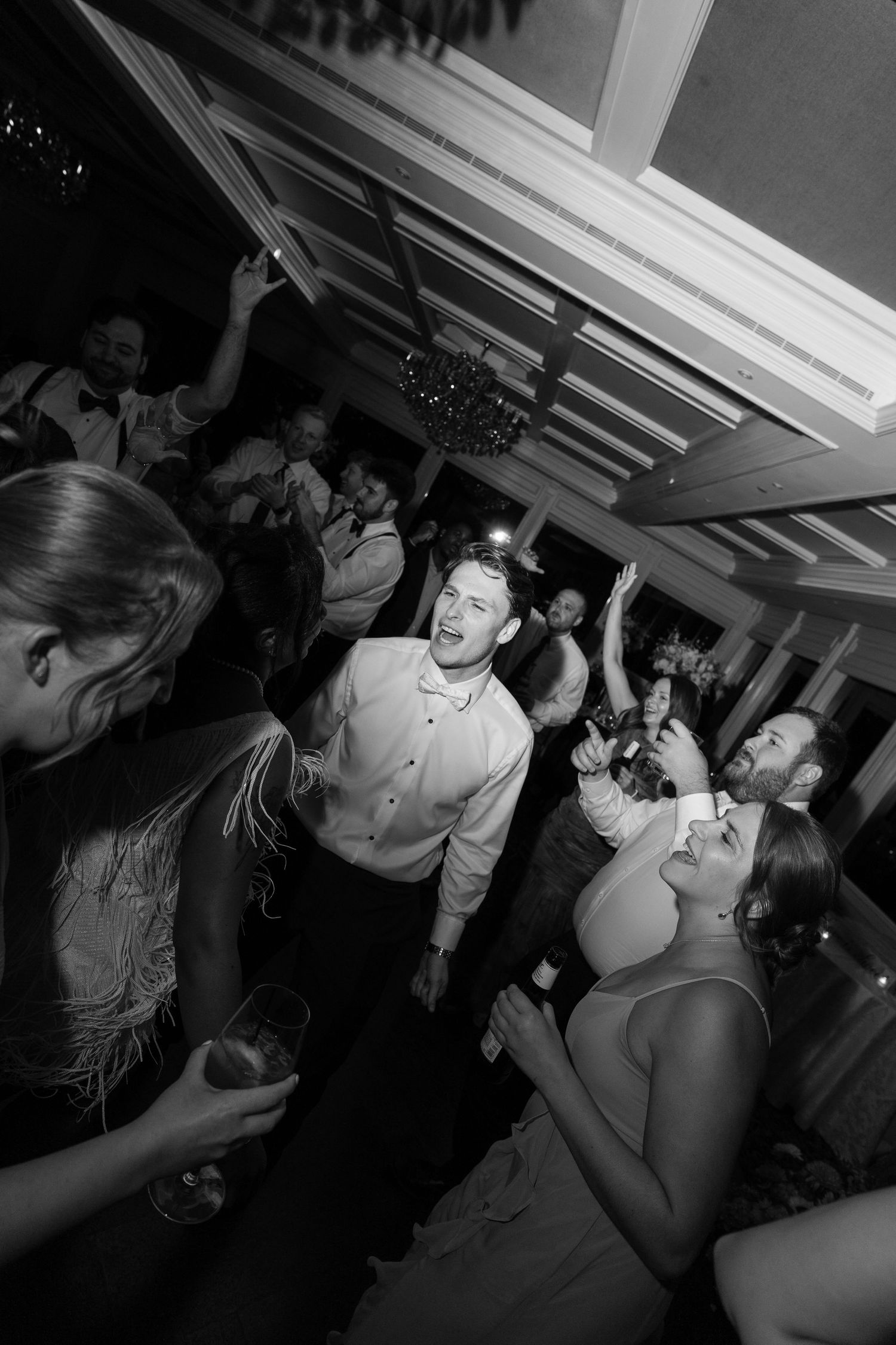 Black and white photo of wedding guests dancing and celebrating energetically on the reception dance floor.