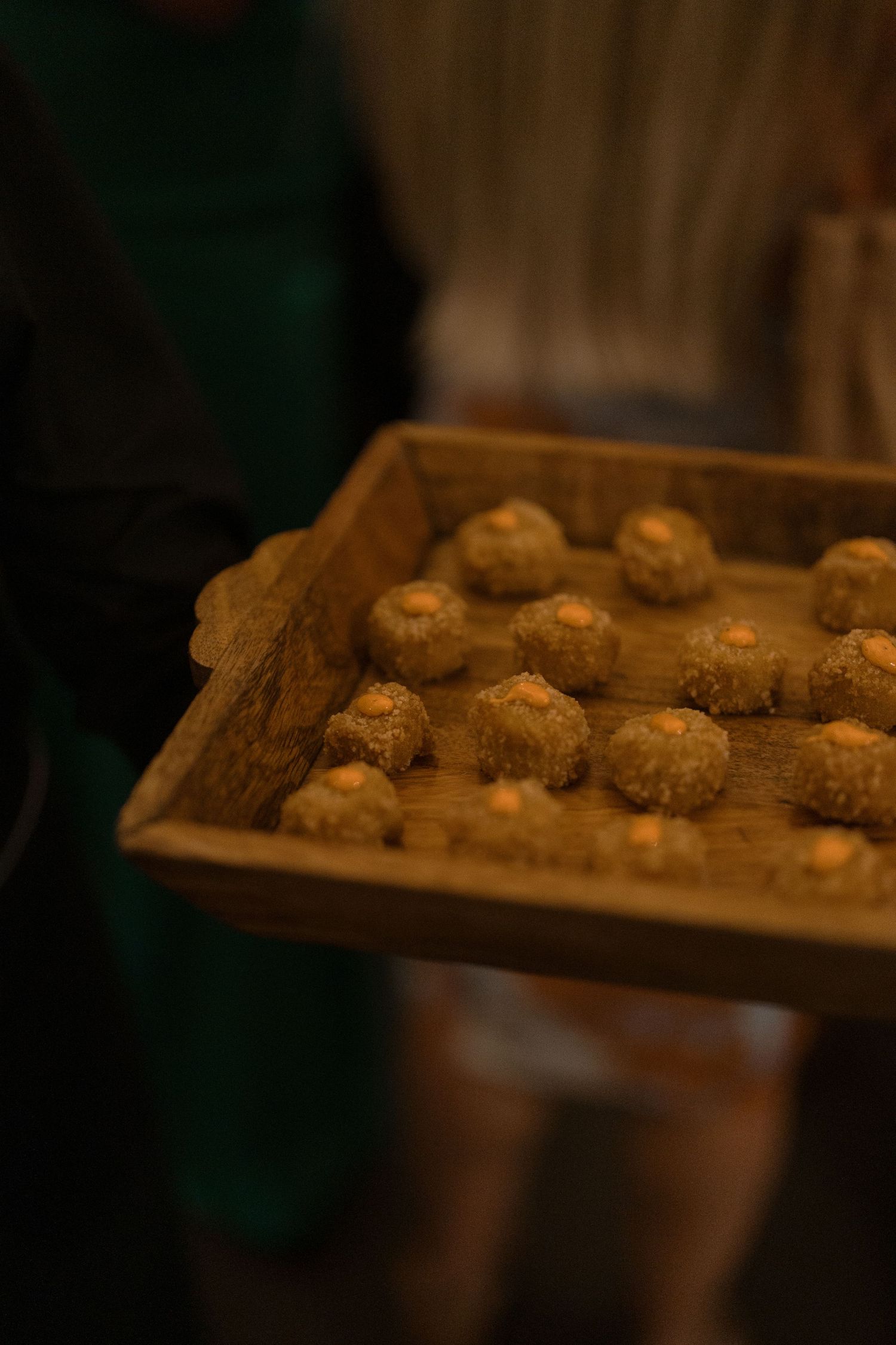 Server presents wooden tray of golden fried appetizer bites at an elegant wedding cocktail hour reception.